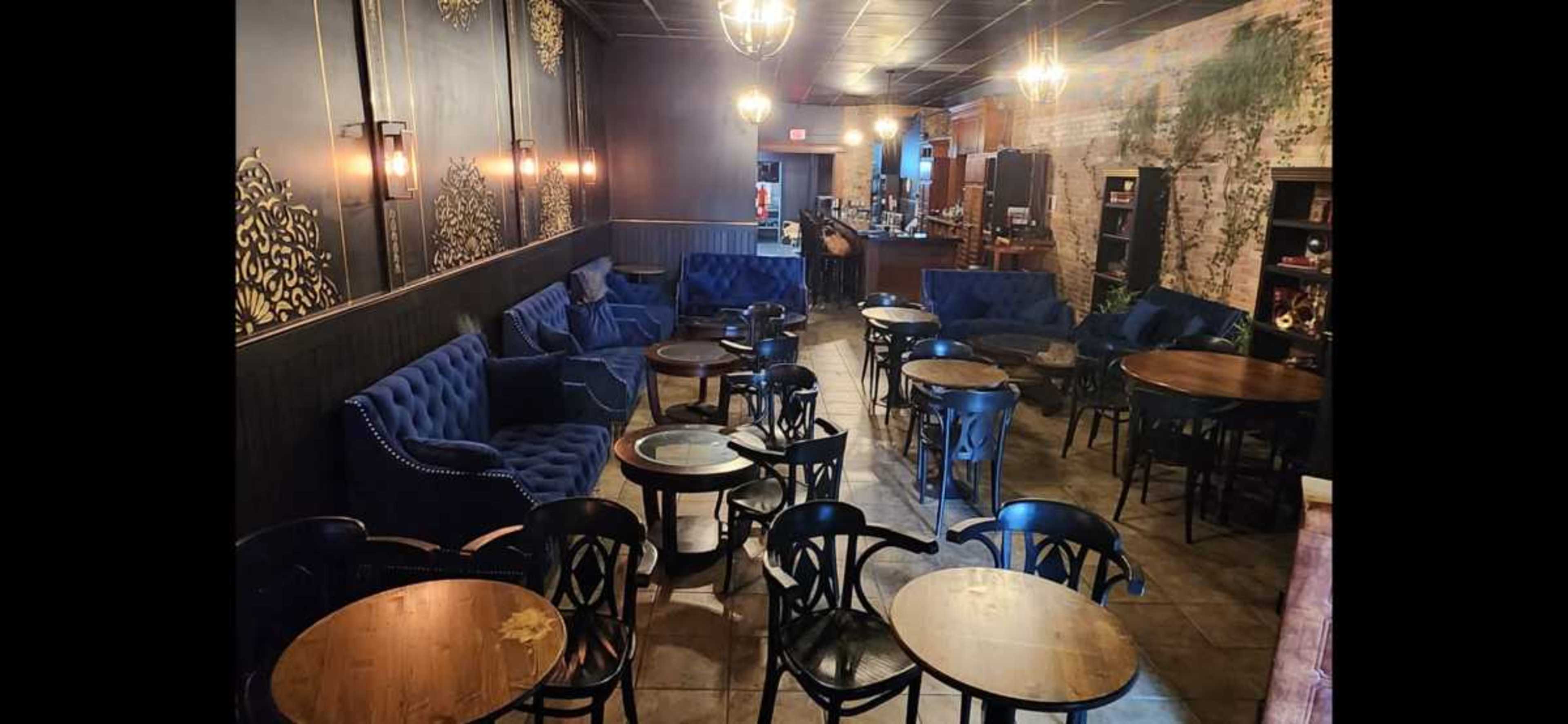 The image shows a cozy cafe interior with blue upholstered seating, wooden tables, and a bar area in the background.