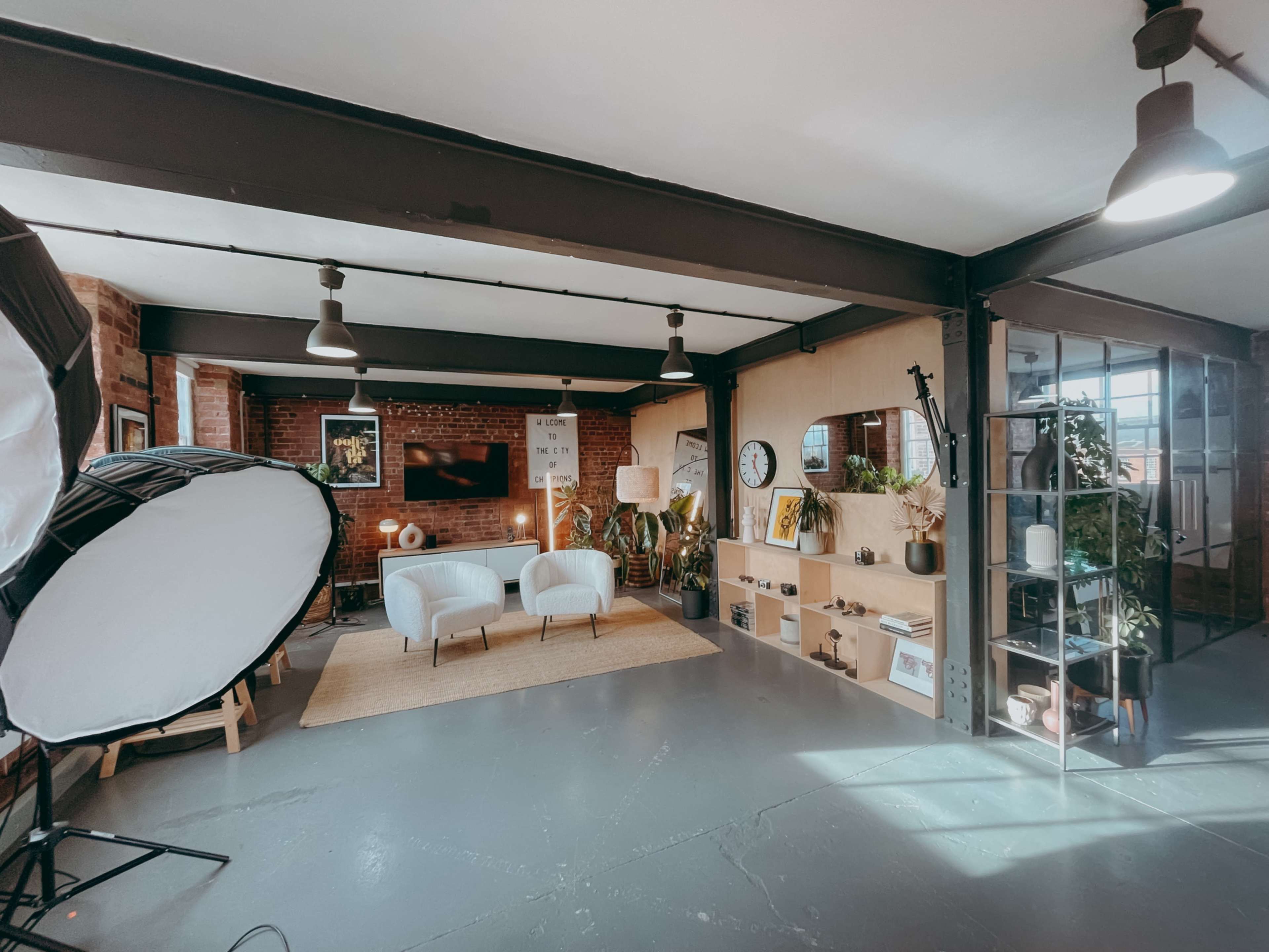 The image shows a spacious, modern interior with exposed brick walls, minimalistic furniture, and a well-organized shelf displaying various decorative items.