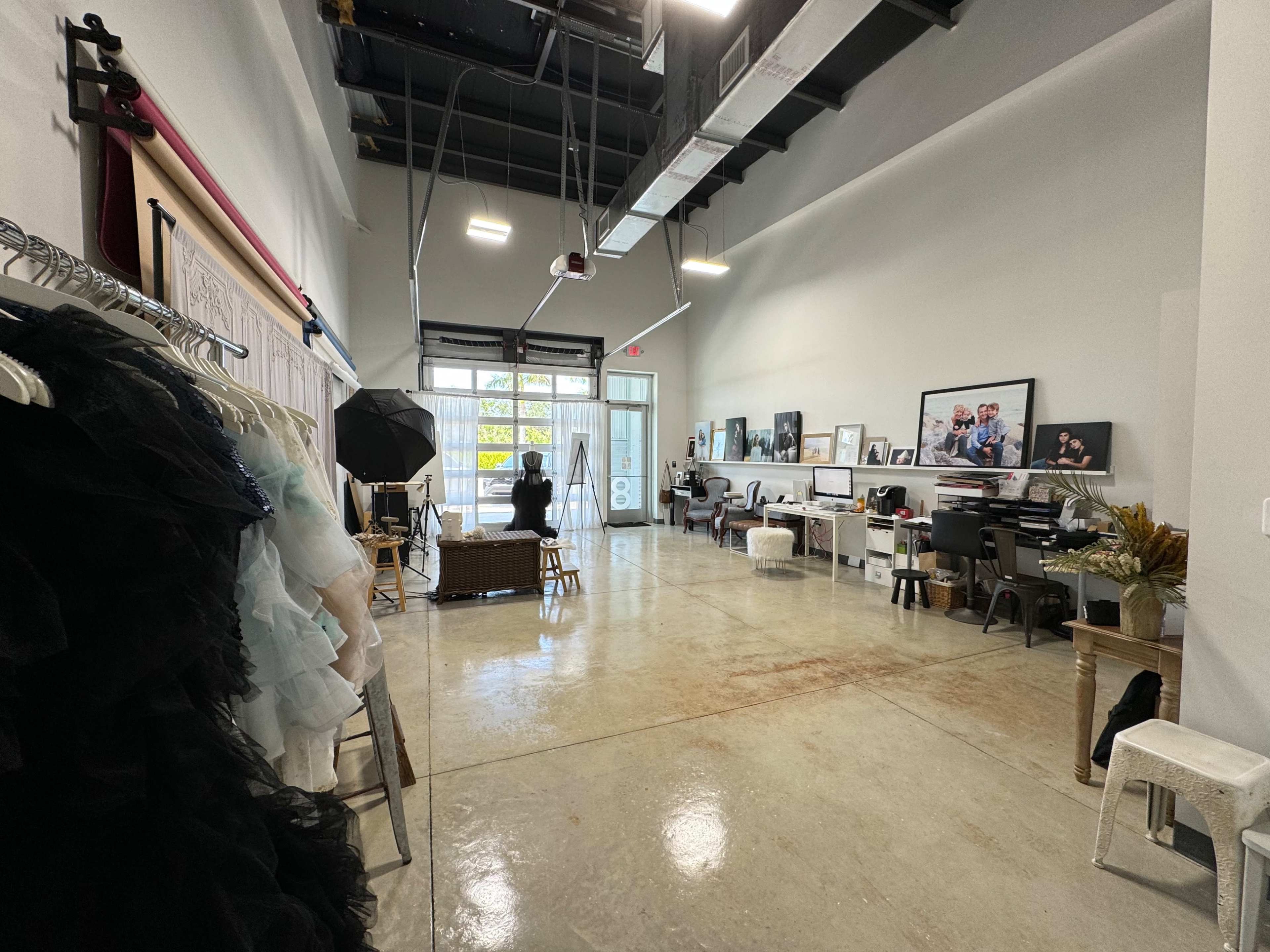 A spacious studio with concrete floors, racks of clothing on one side, and workstations set up against the walls.