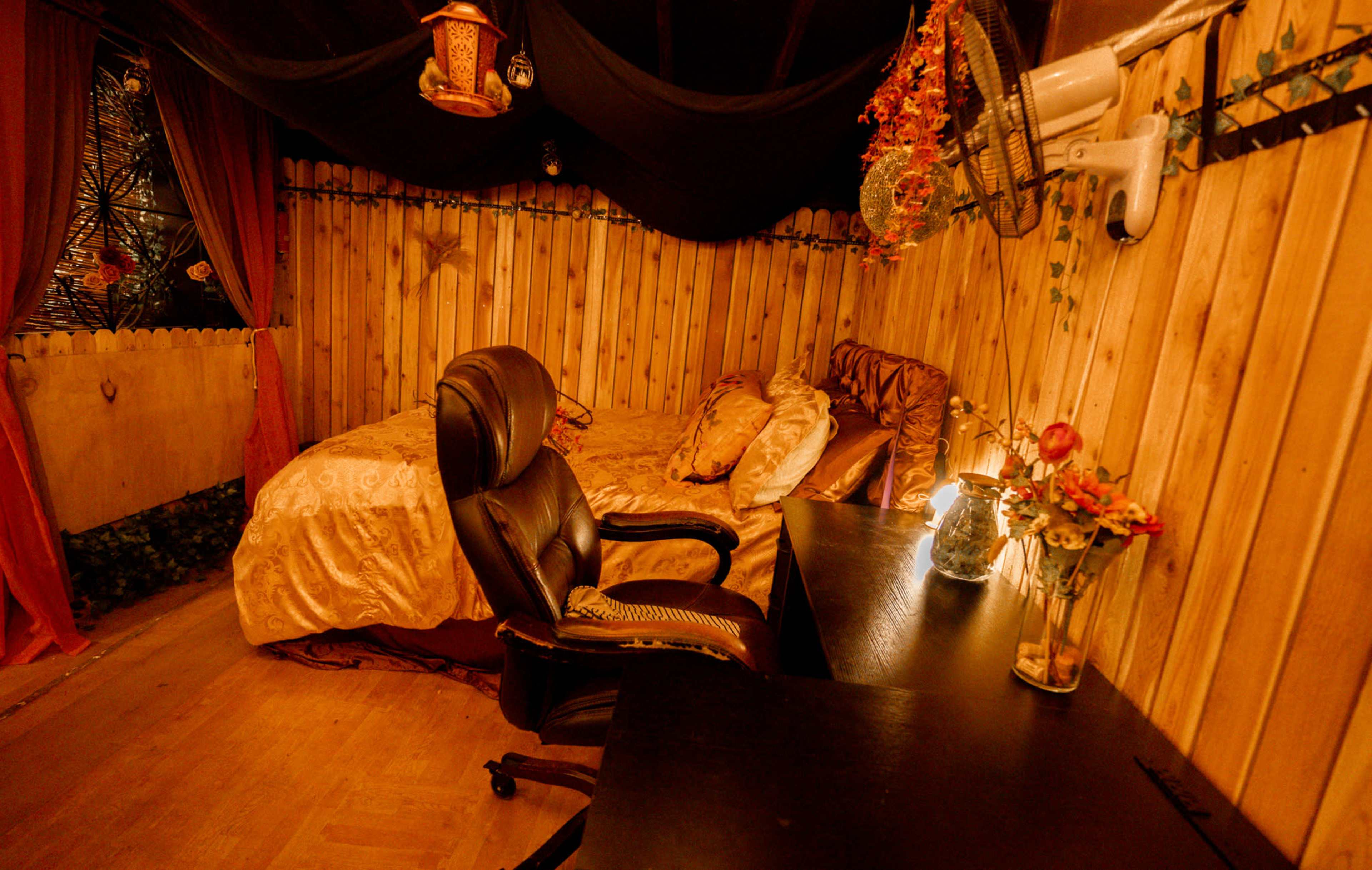 The image shows a cozy wooden room with a bed, a desk, and decorative elements like flowers and hanging lanterns.