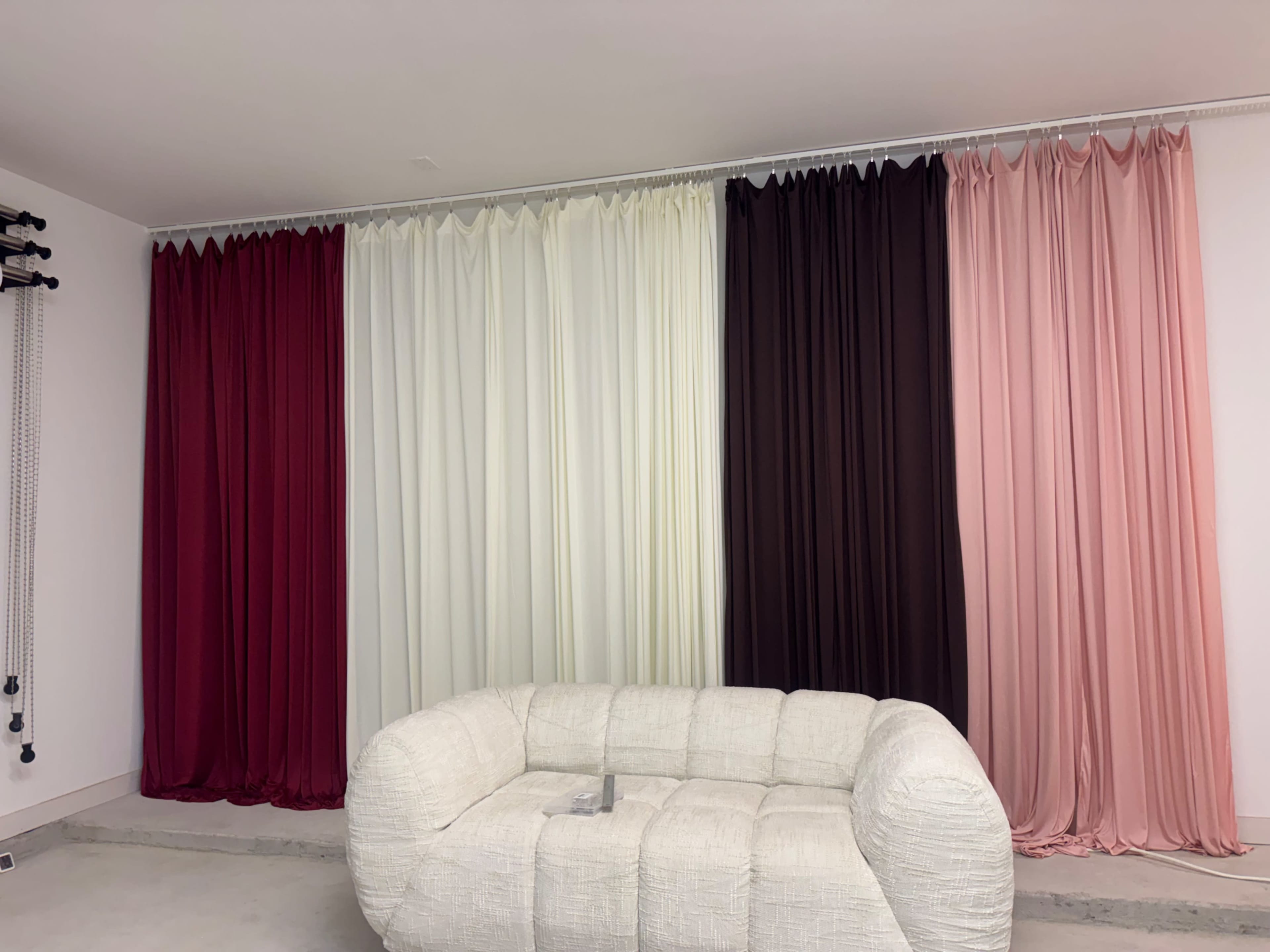 The image shows a modern room with a white, textured sofa in front of a wall adorned with curtains in varying colors, including red, white, black, and pink.