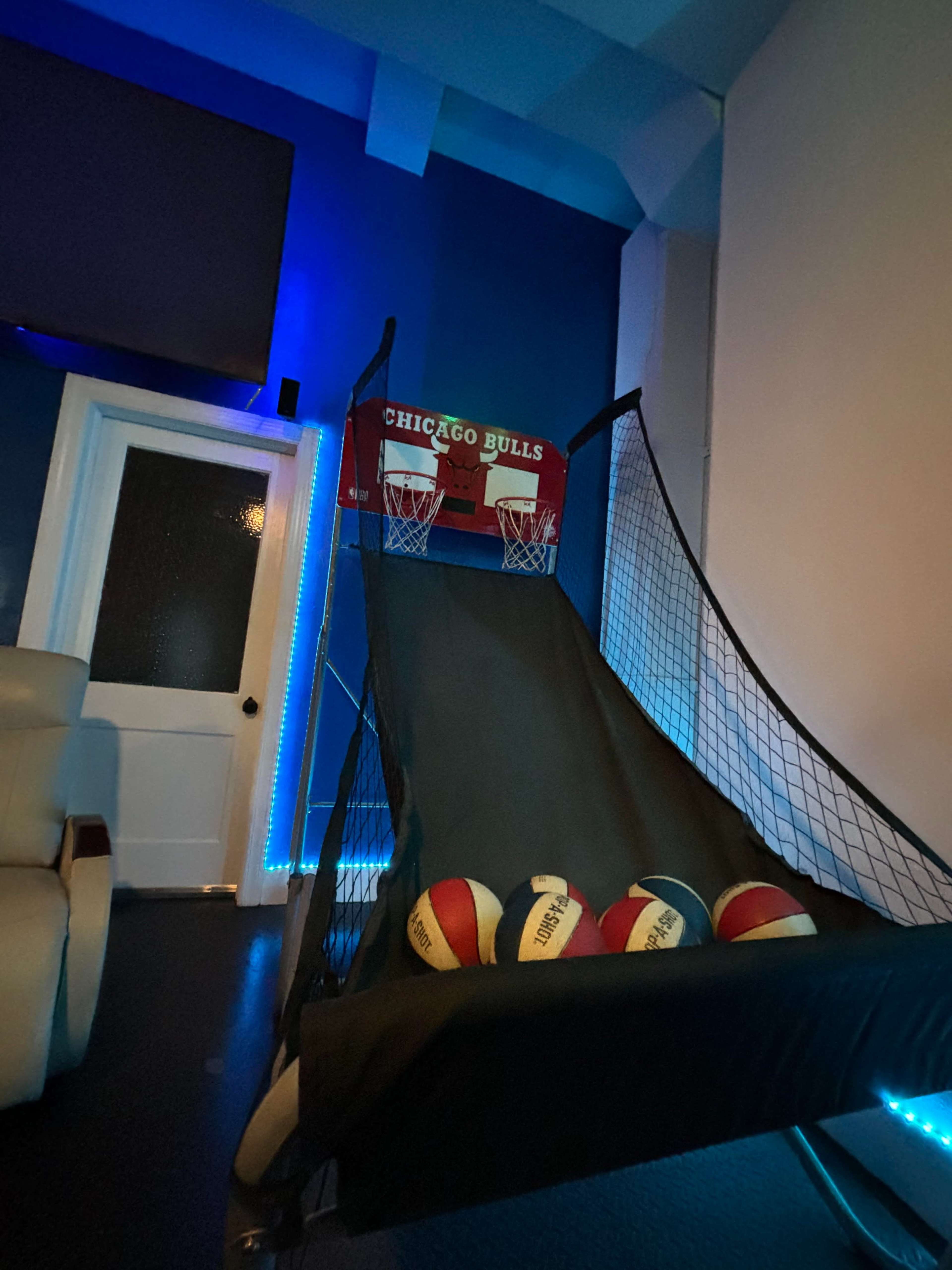 The image shows a basketball shooting arcade game decorated with Chicago Bulls branding, positioned against a blue wall with several basketballs resting in its netted section.