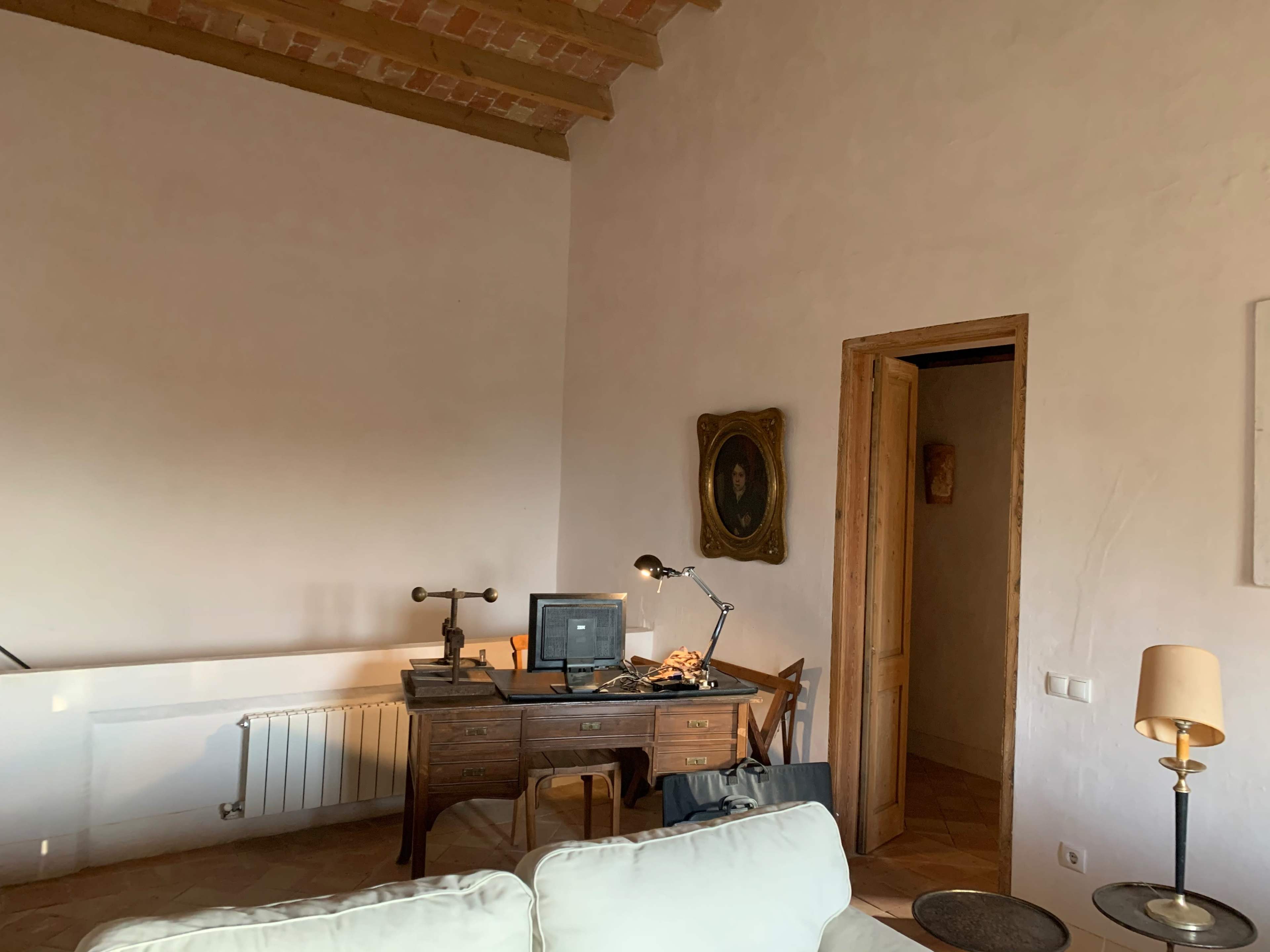 A minimalist room with a wooden desk, a computer monitor, a lamp, and a door leading to another space.