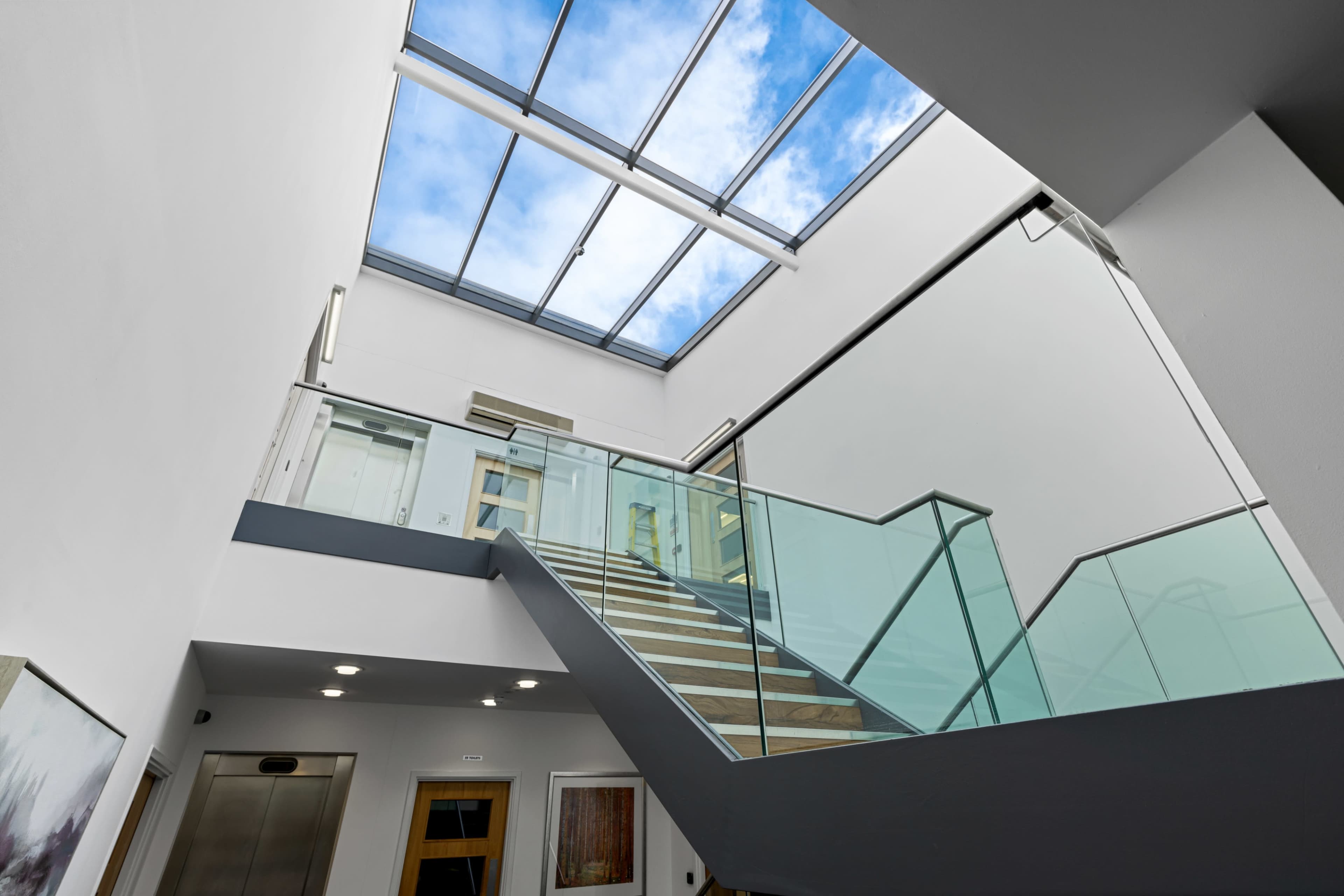 A modern staircase with glass railings leads to a skylight, allowing natural light to illuminate the interior space.
