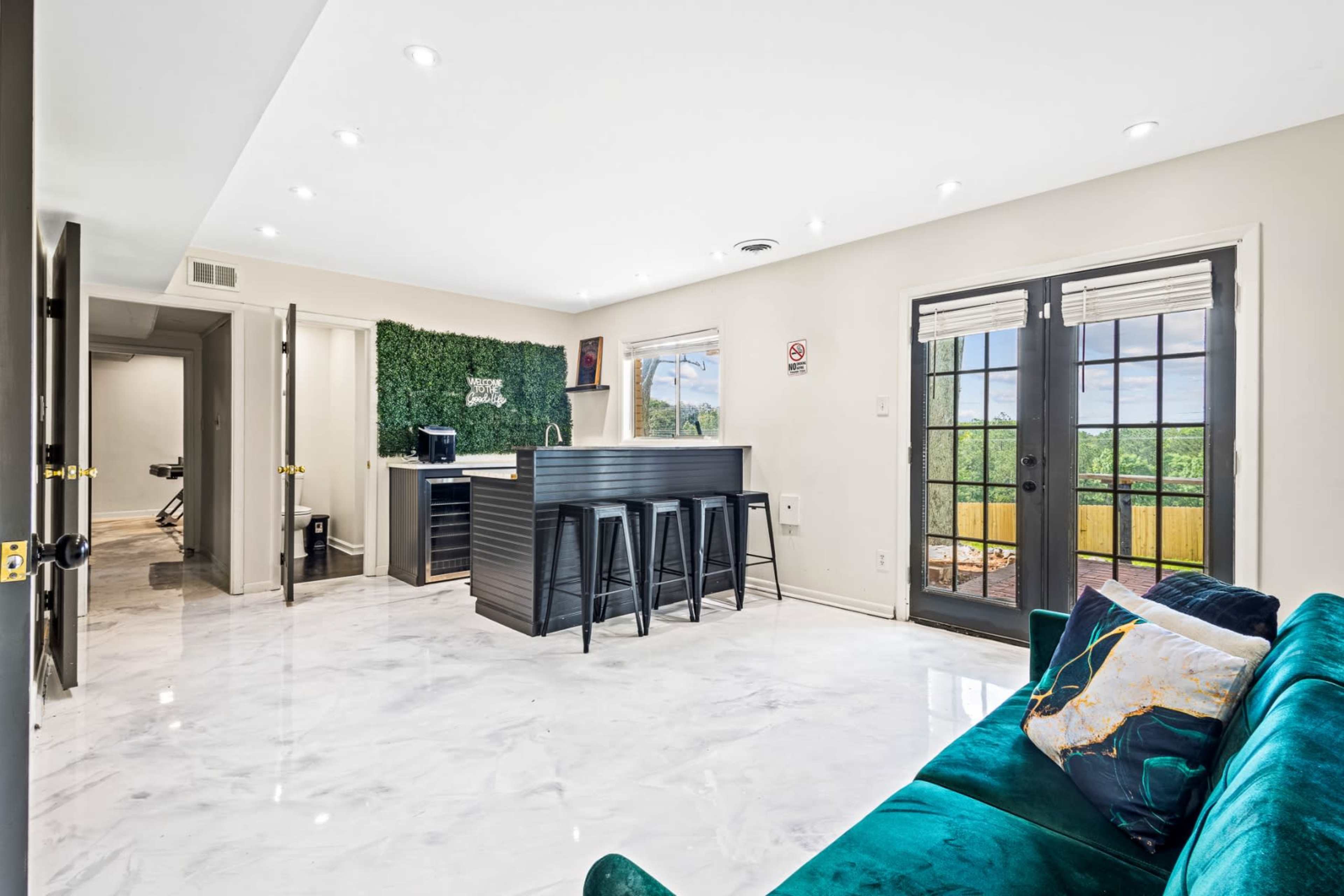 The image shows a modern living space featuring a marble floor, a green accent wall, a black kitchen island with stools, and large glass doors leading to an outdoor view.