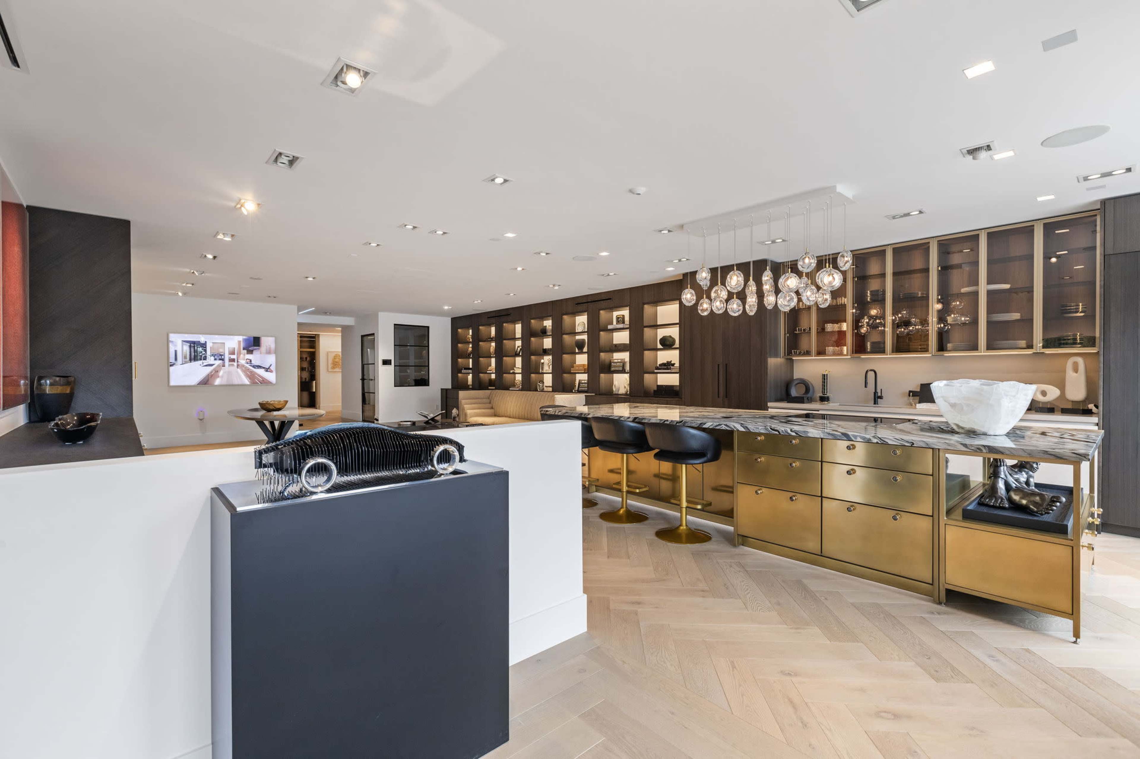 A modern kitchen and living area with a sleek design, featuring a large island, golden cabinetry, and illuminated shelves.