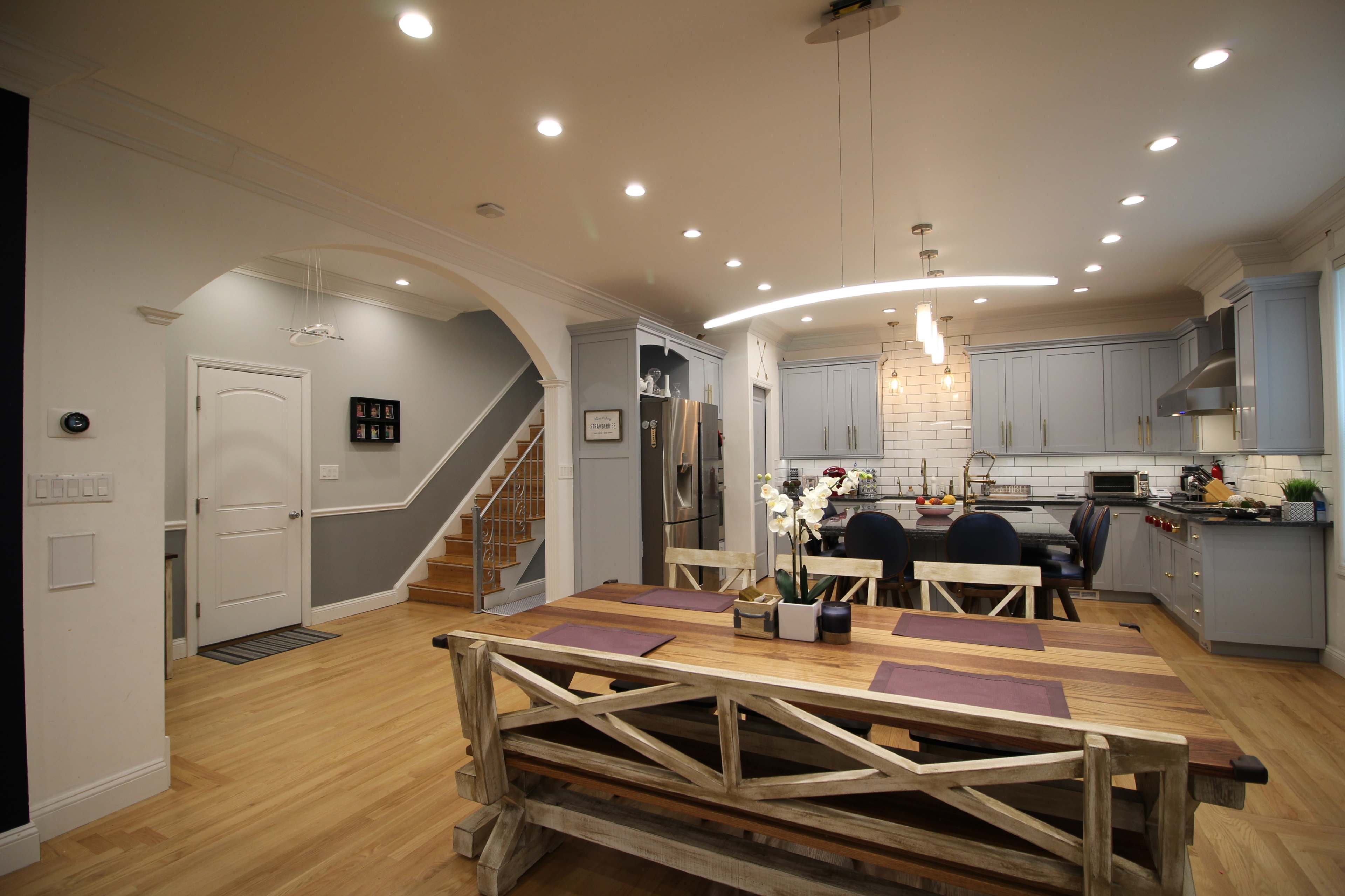 A modern kitchen and dining area with a wooden table, blue cabinetry, and a staircase leading to an upper level.
