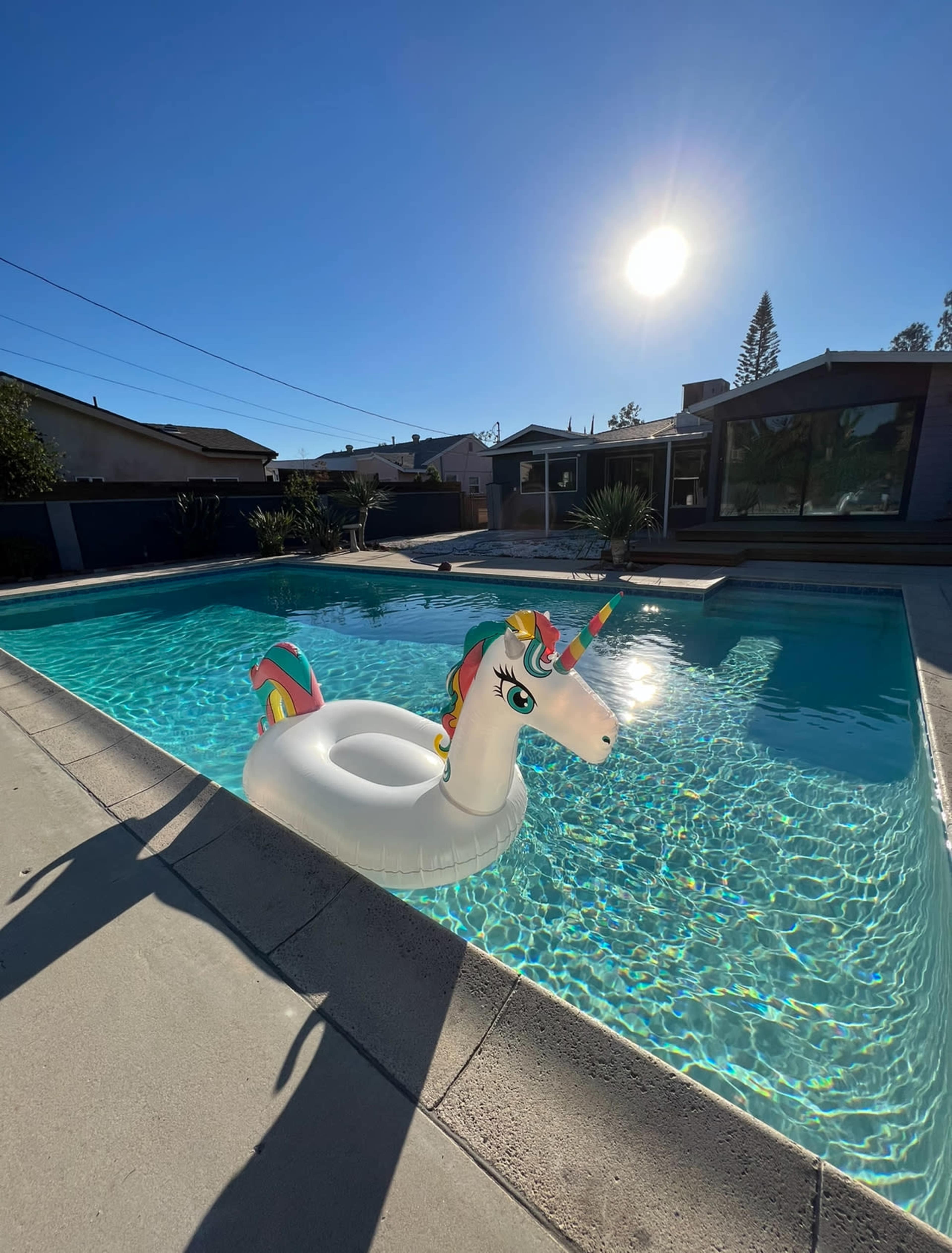 A unicorn-shaped float sits in a clear swimming pool under a bright sun.