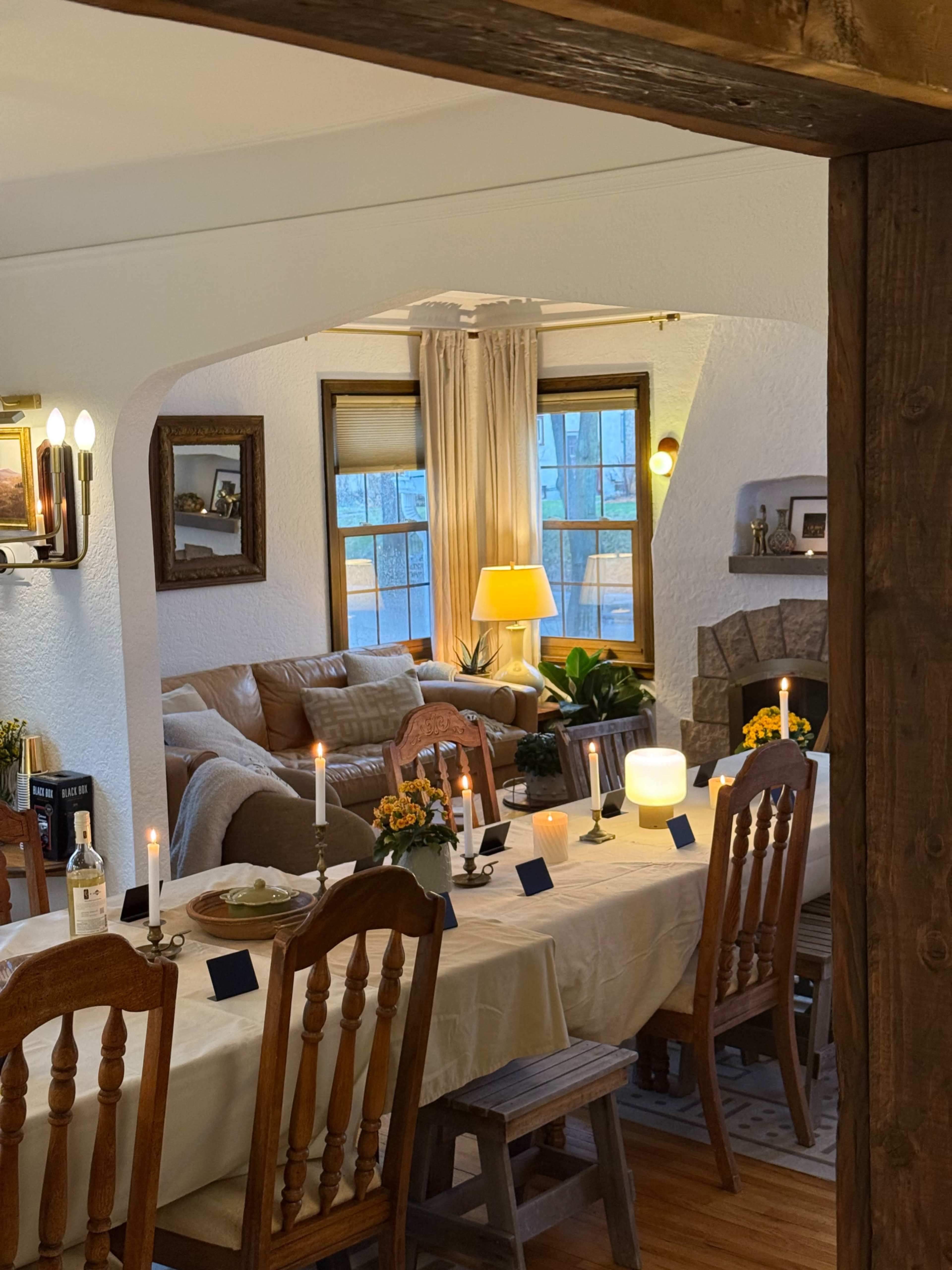 A dining room is set with candles and flowers, with a cozy living area visible in the background.