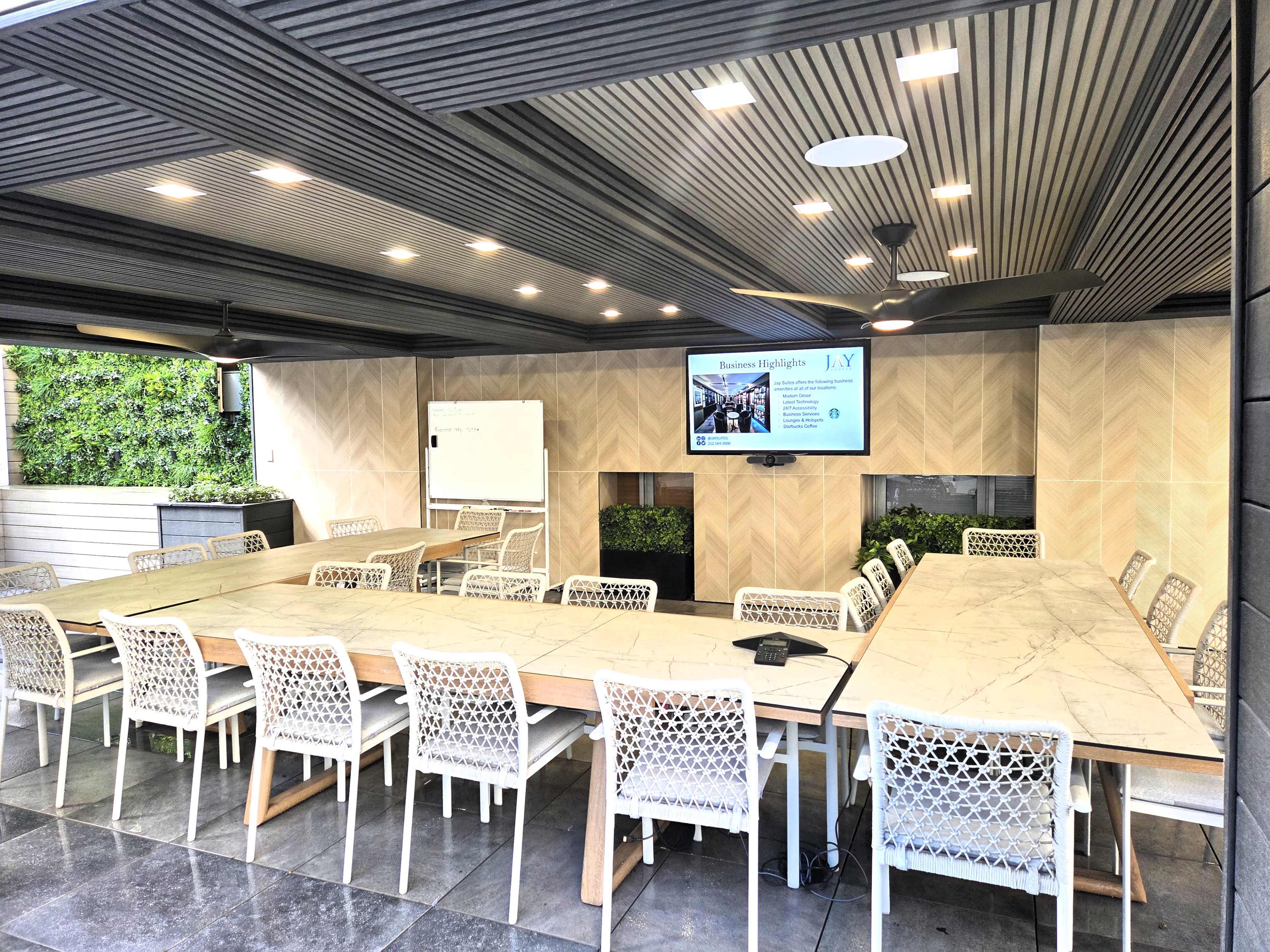 A modern conference room features a large table surrounded by white chairs, with a wall-mounted screen and a whiteboard in a well-lit space.