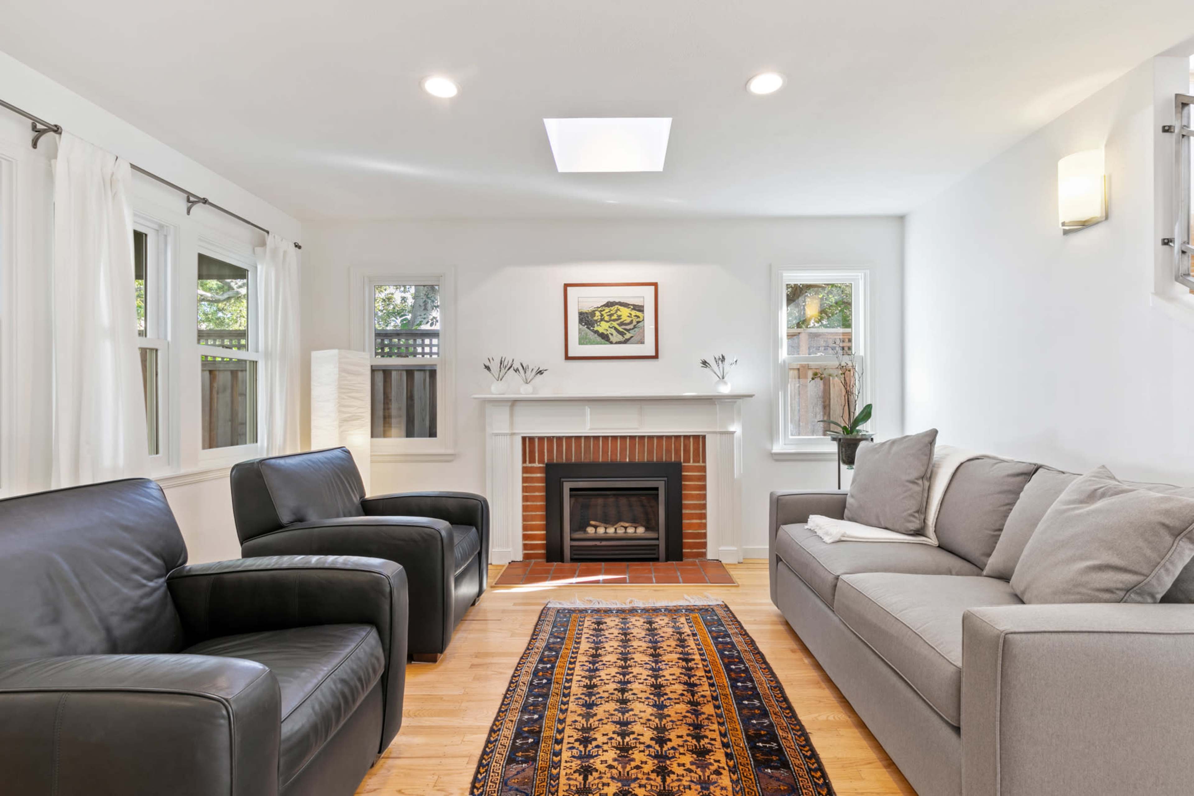 A modern living room featuring a fireplace, two armchairs, a gray sofa, hardwood floors, and a decorative area rug.