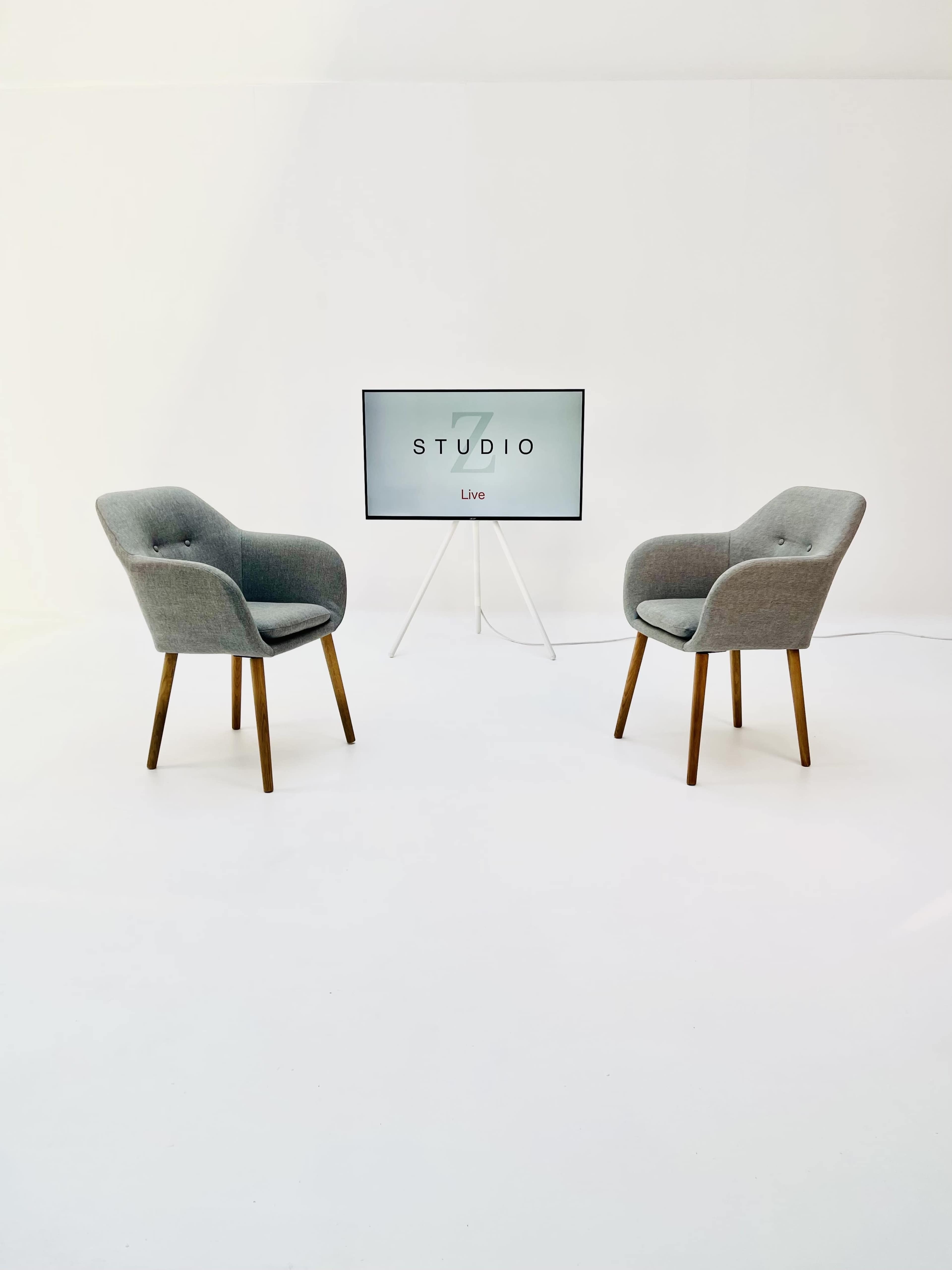 A minimalist studio setup with two gray chairs facing a television screen displaying the word "STUDIO" and "Live."