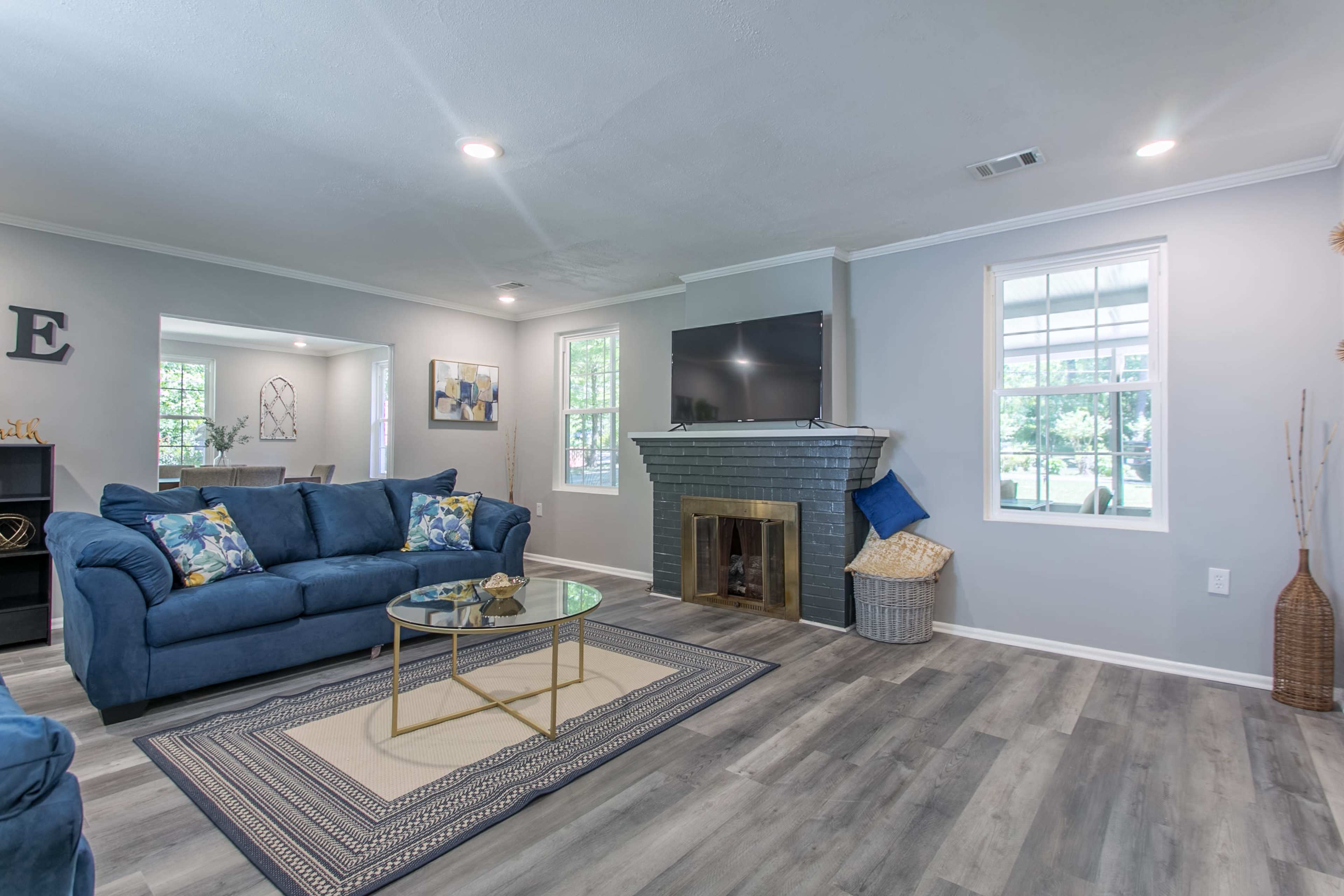 The living room features a blue sectional sofa, a glass coffee table, and a fireplace with a mounted television above it, surrounded by light-colored walls and hardwood flooring.