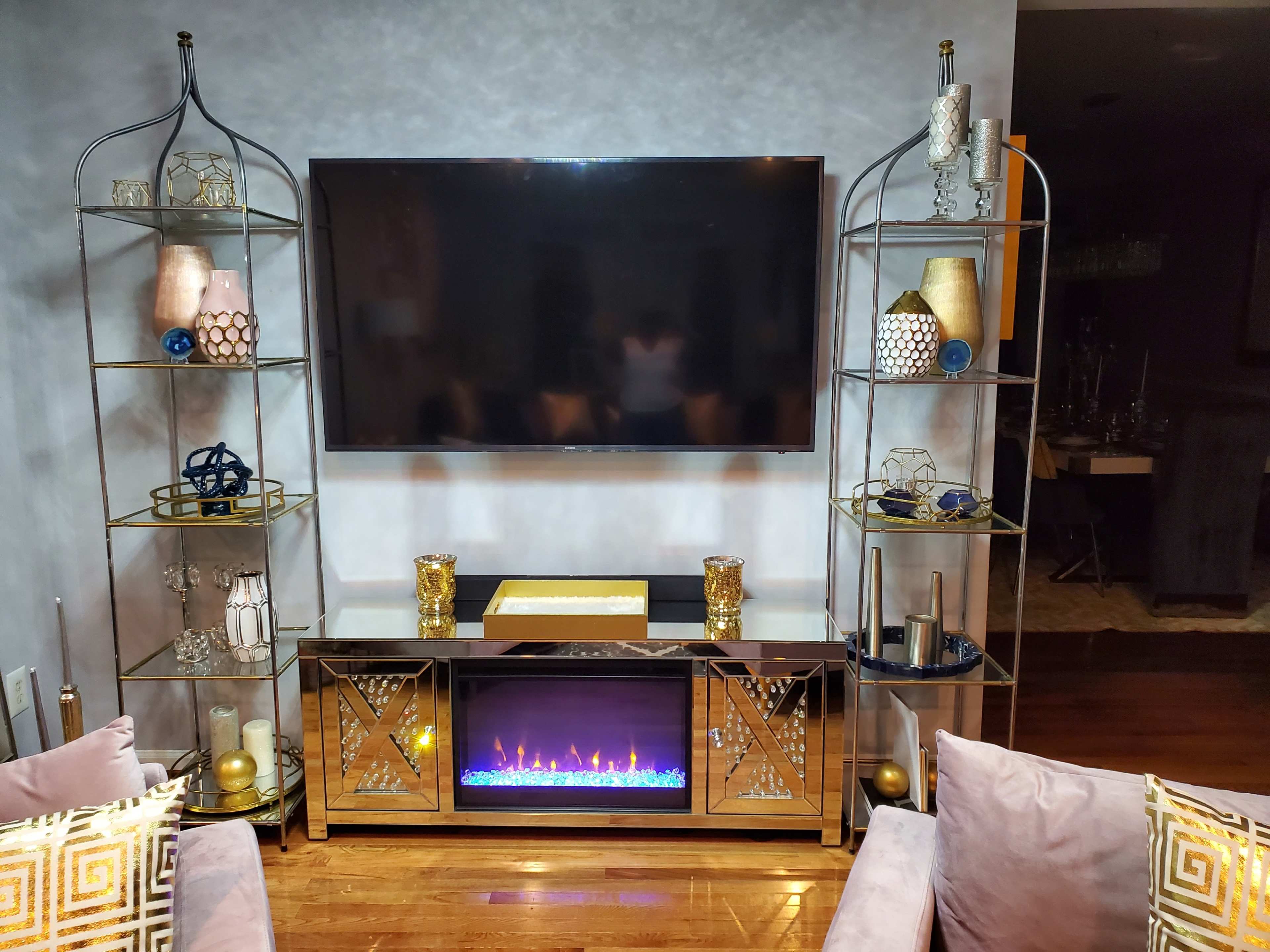A living room with a wall-mounted TV above a decorative entertainment center featuring a glowing electric fireplace and stylish shelving units on either side.