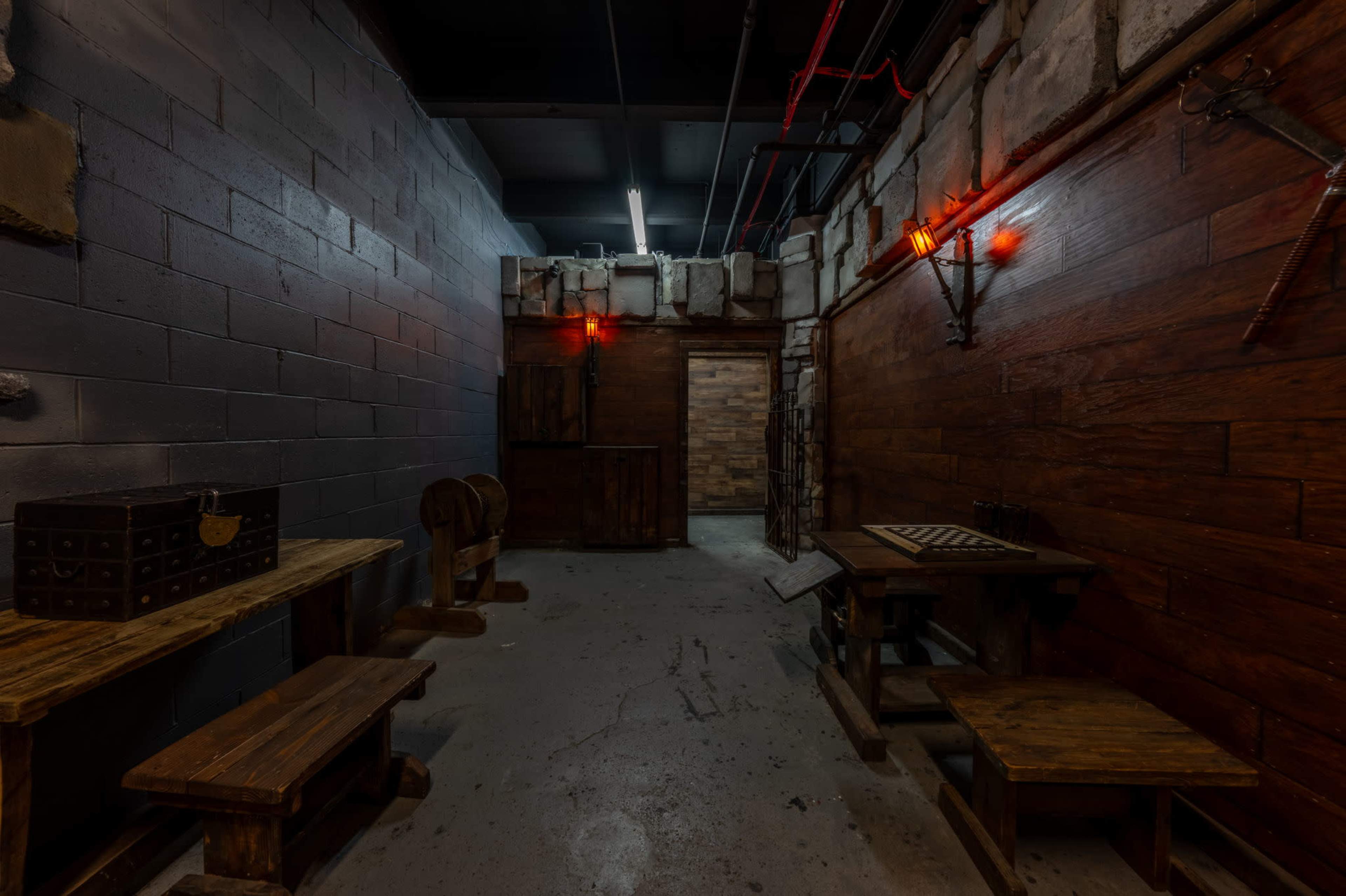 The image shows a dimly lit corridor with wooden walls, a wooden table and benches on one side, and a door at the end leading to another room.