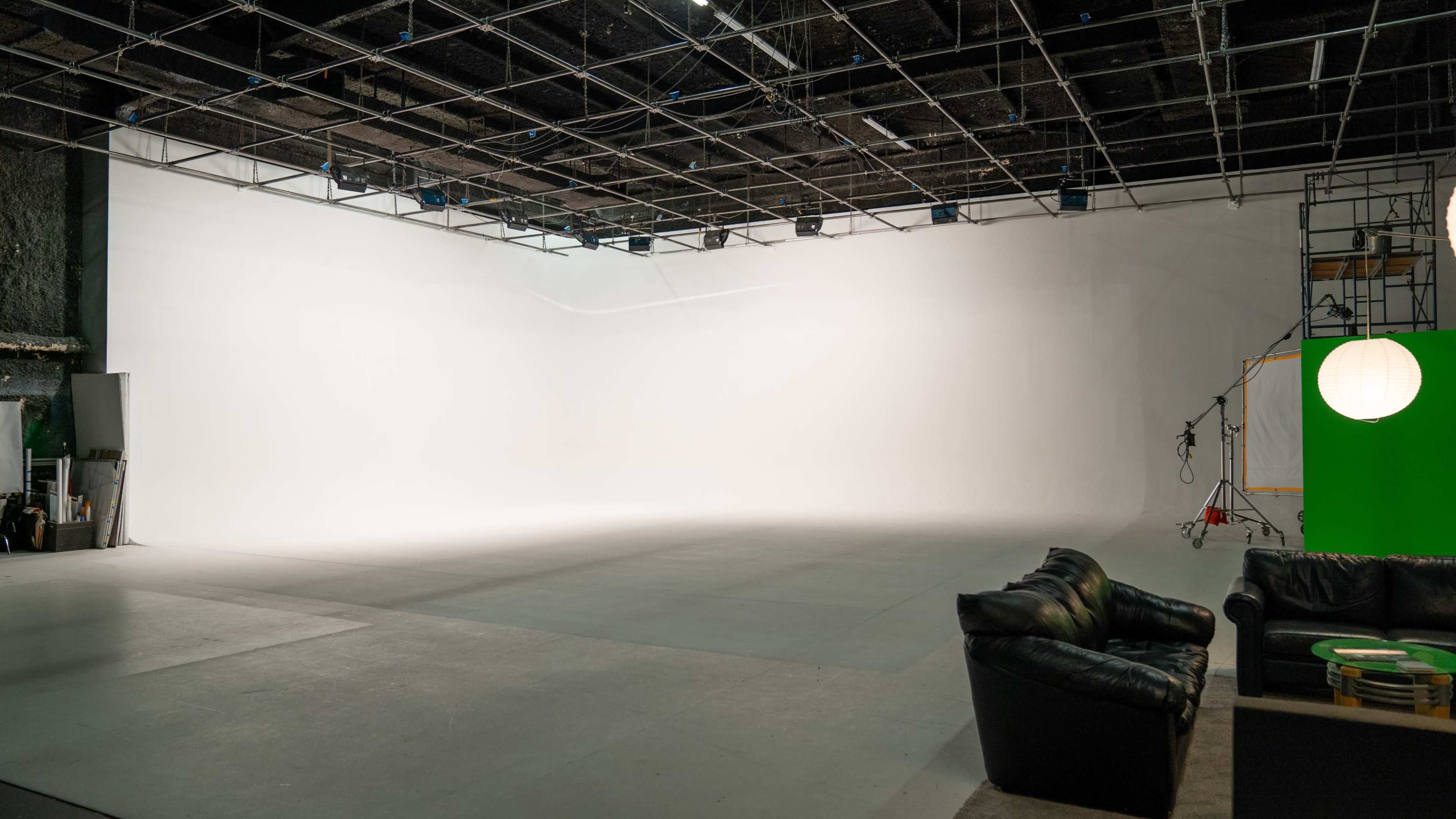 An empty studio space with a white backdrop and minimal furniture in the foreground.