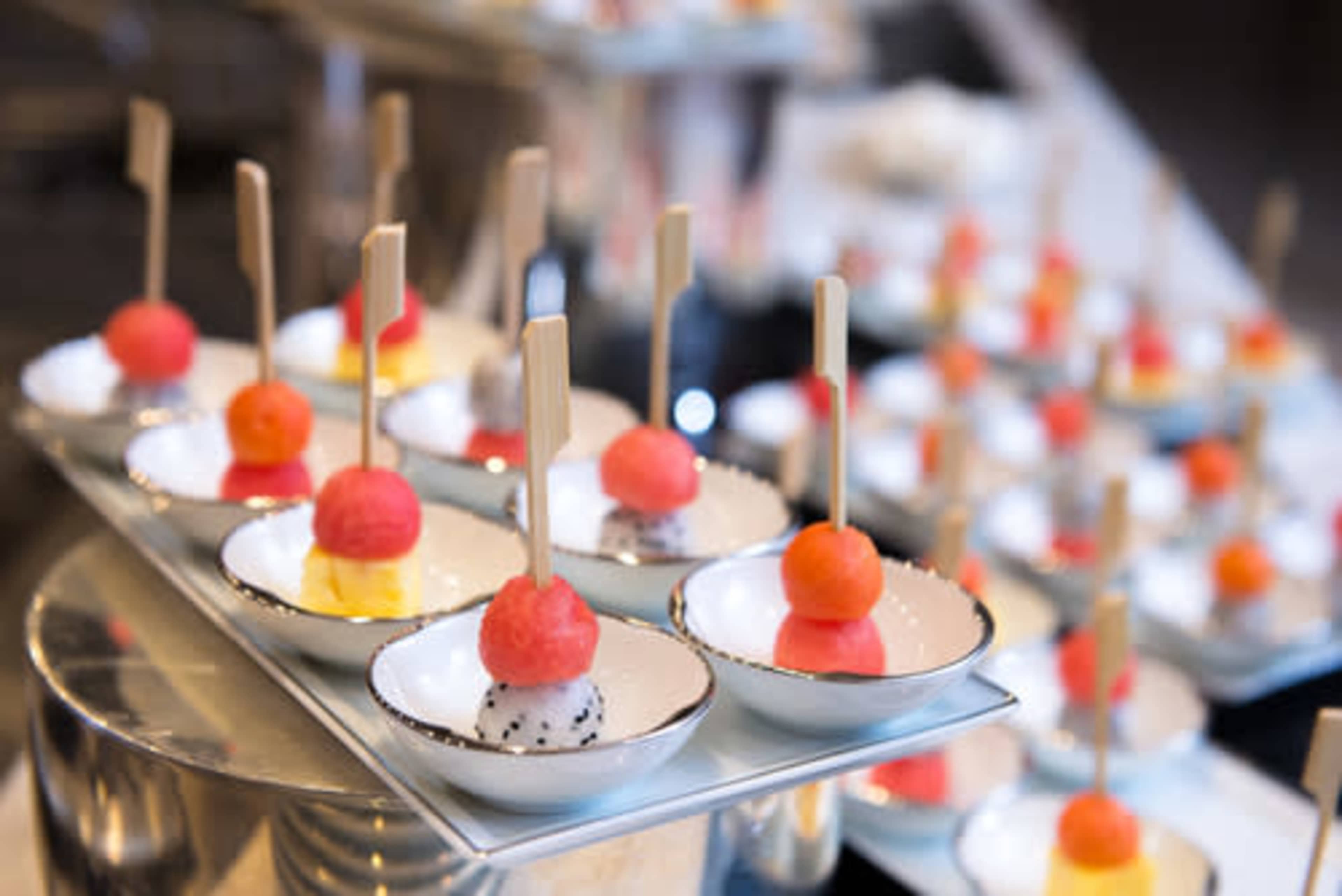 Small scoops of colorful sorbet served in white bowls, each topped with a wooden stick.