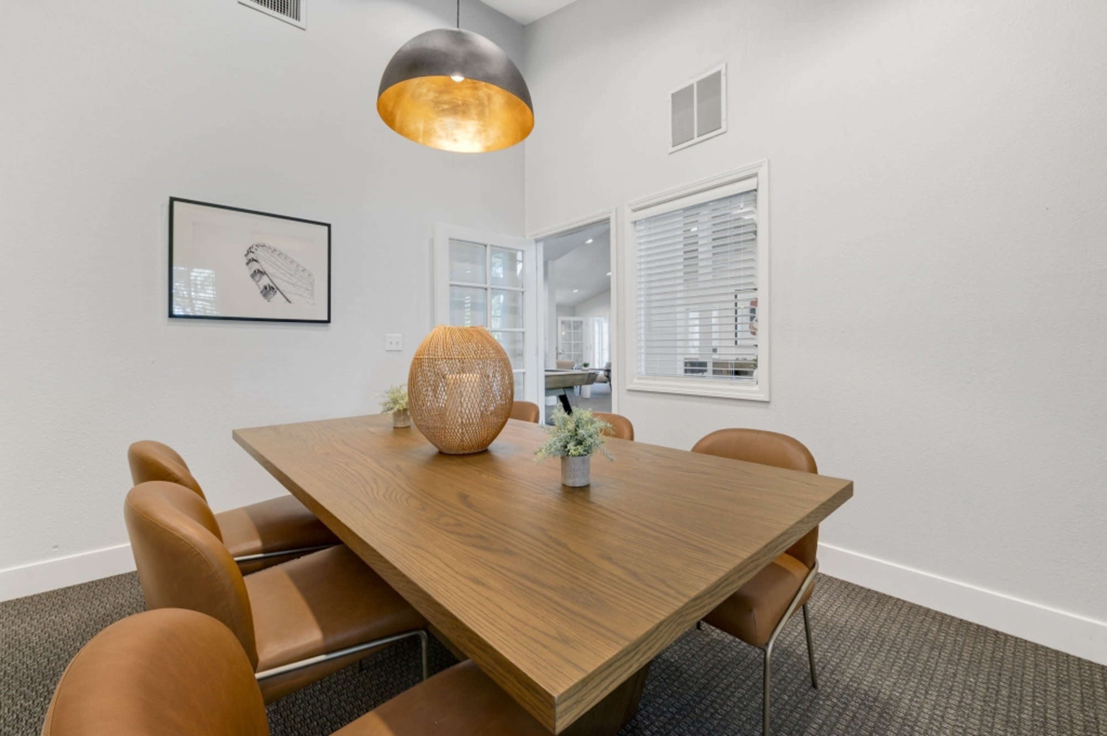 A wooden dining table is surrounded by leather chairs in a well-lit room with a pendant light and decorative vase.