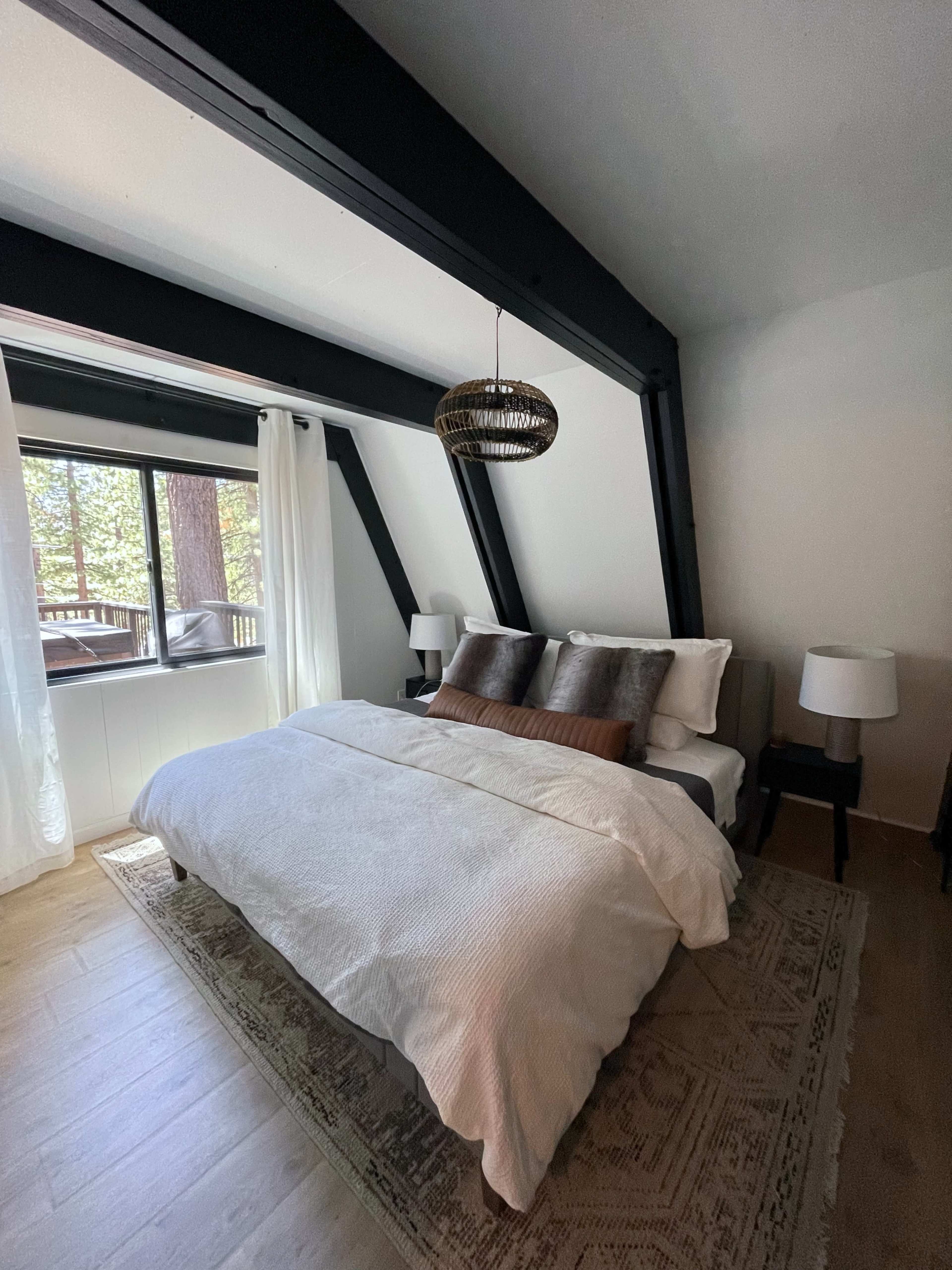 A minimalist bedroom with a bed, two bedside tables, and large windows overlooking a forested area.