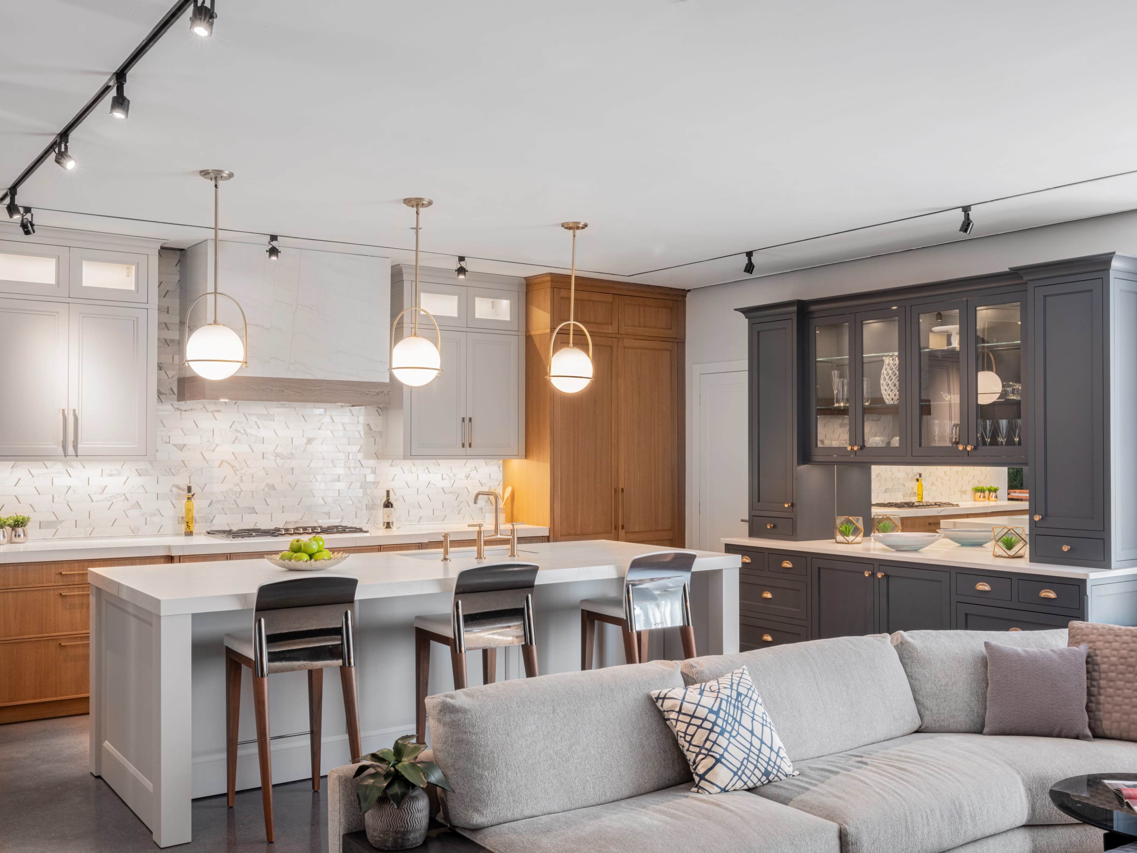 A modern kitchen features a large island with seating, wooden and gray cabinetry, pendant lighting, and a stylish backsplash.