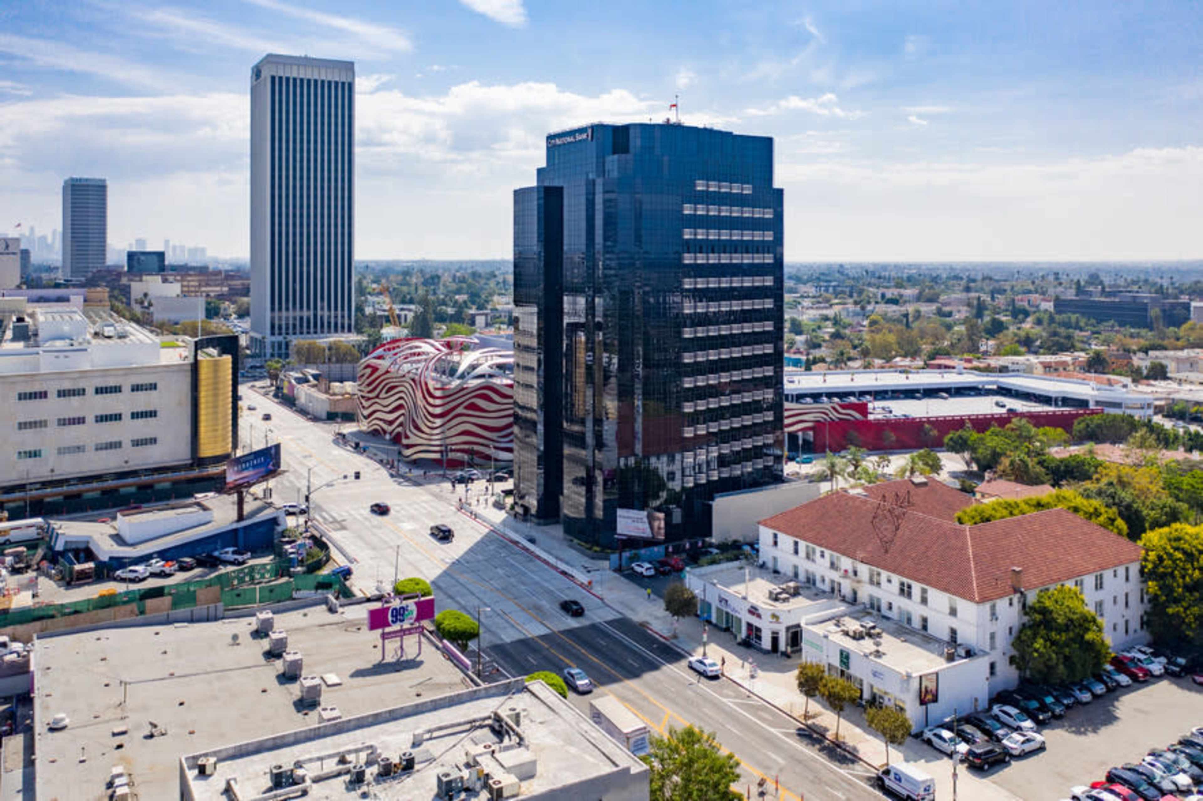 The image shows a cityscape featuring modern buildings, including a black high-rise and a uniquely designed structure with wavy red and white patterns, amidst a busy street lined with vehicles.