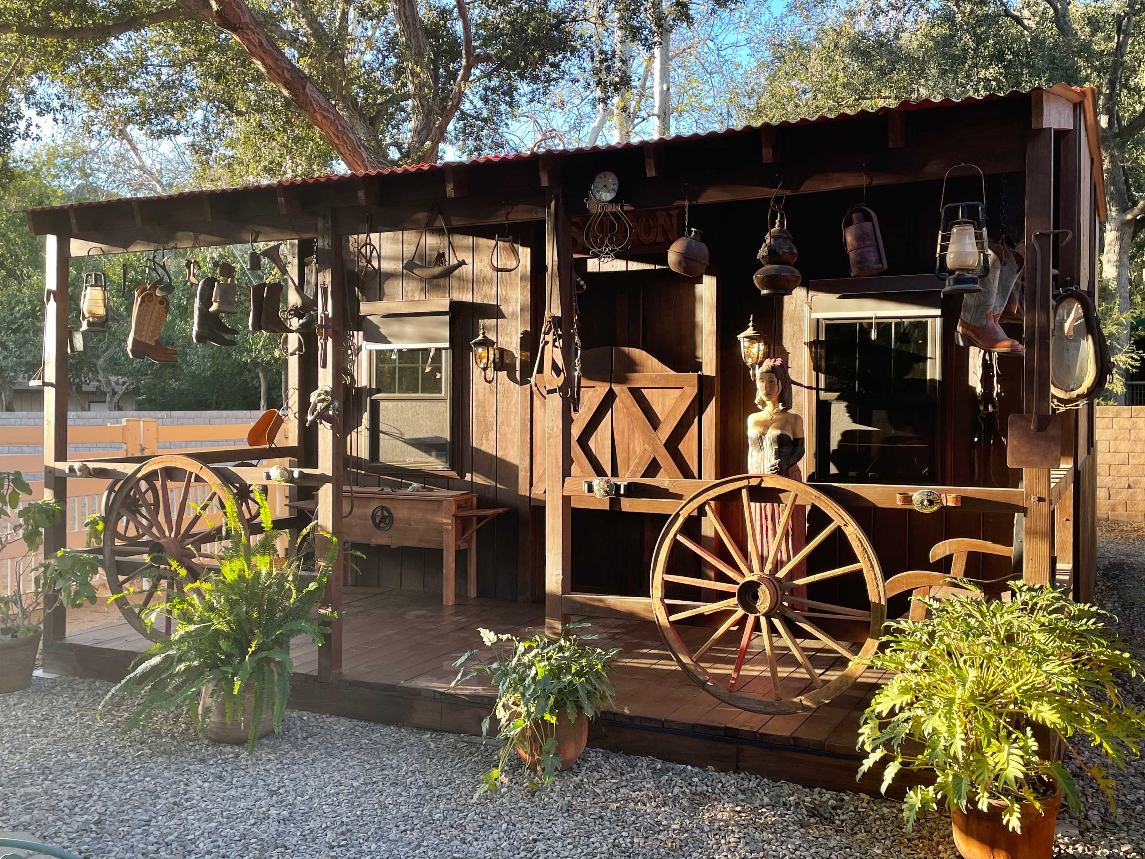 A wooden structure resembling a rustic storehouse displays various antique lanterns and decor, with two large wheels positioned at the front.