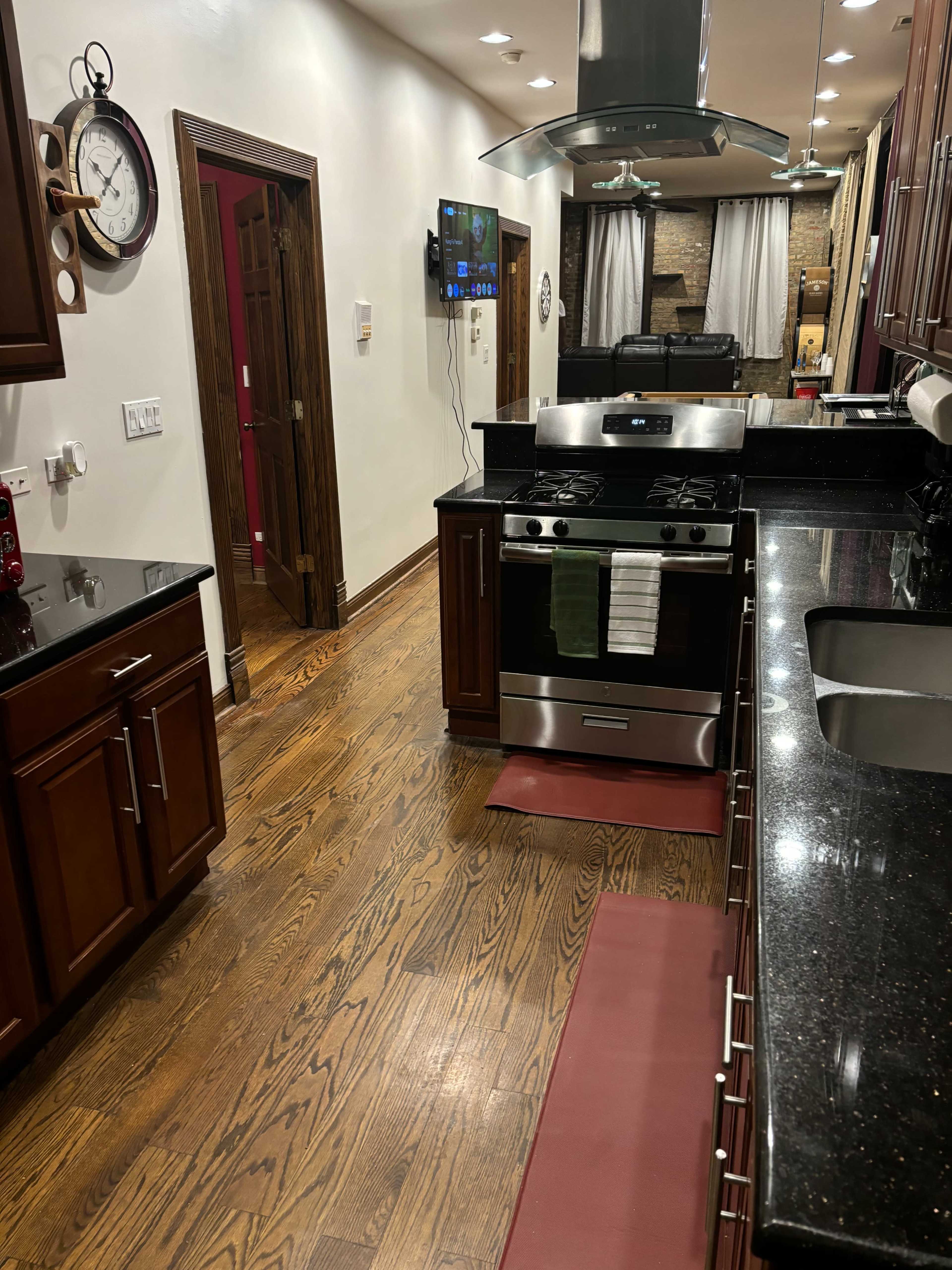 The image shows a modern kitchen with dark wood cabinets, a stainless steel stove, and a view of a living area in the background.