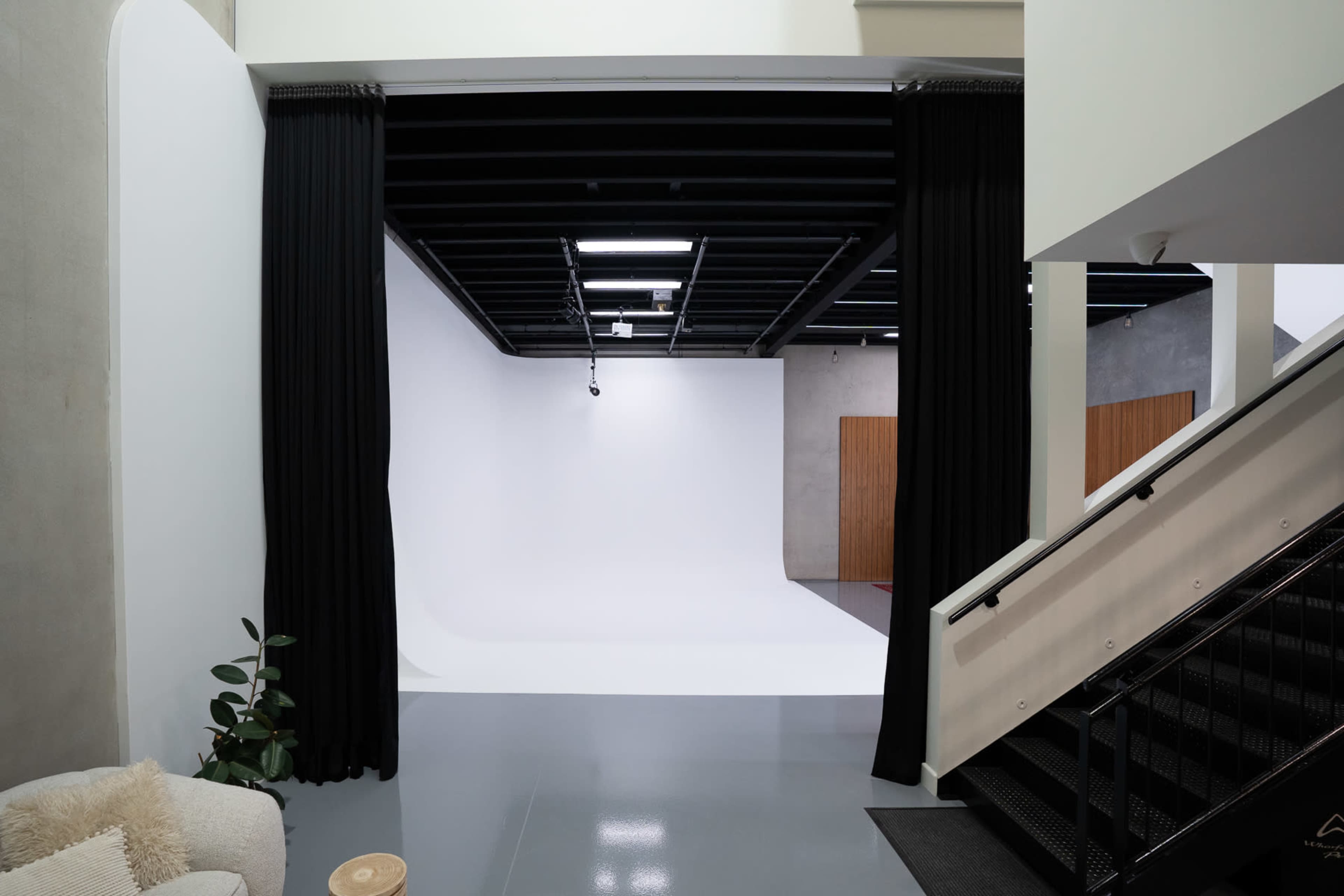 The image shows an open space with a stairway leading down to a bright studio area framed by black curtains.
