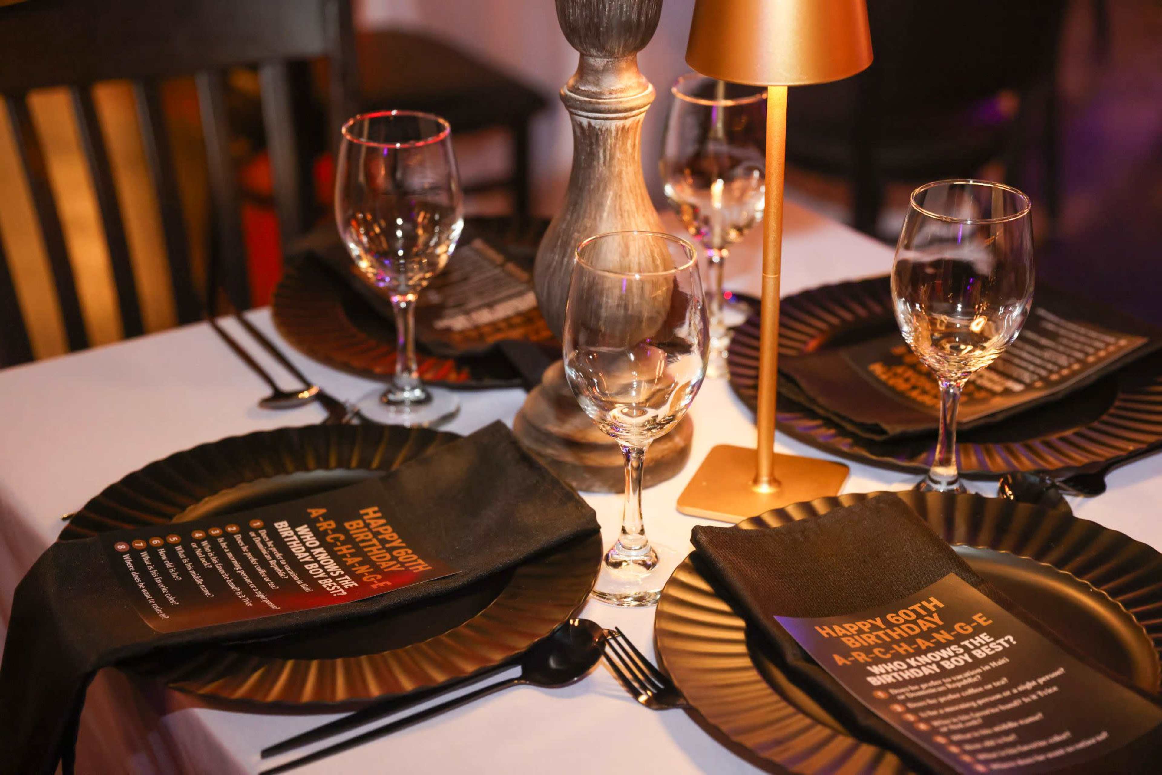 A beautifully arranged dining table features black plates, wine glasses, and decorative napkins with birthday messages, alongside a candle holder.