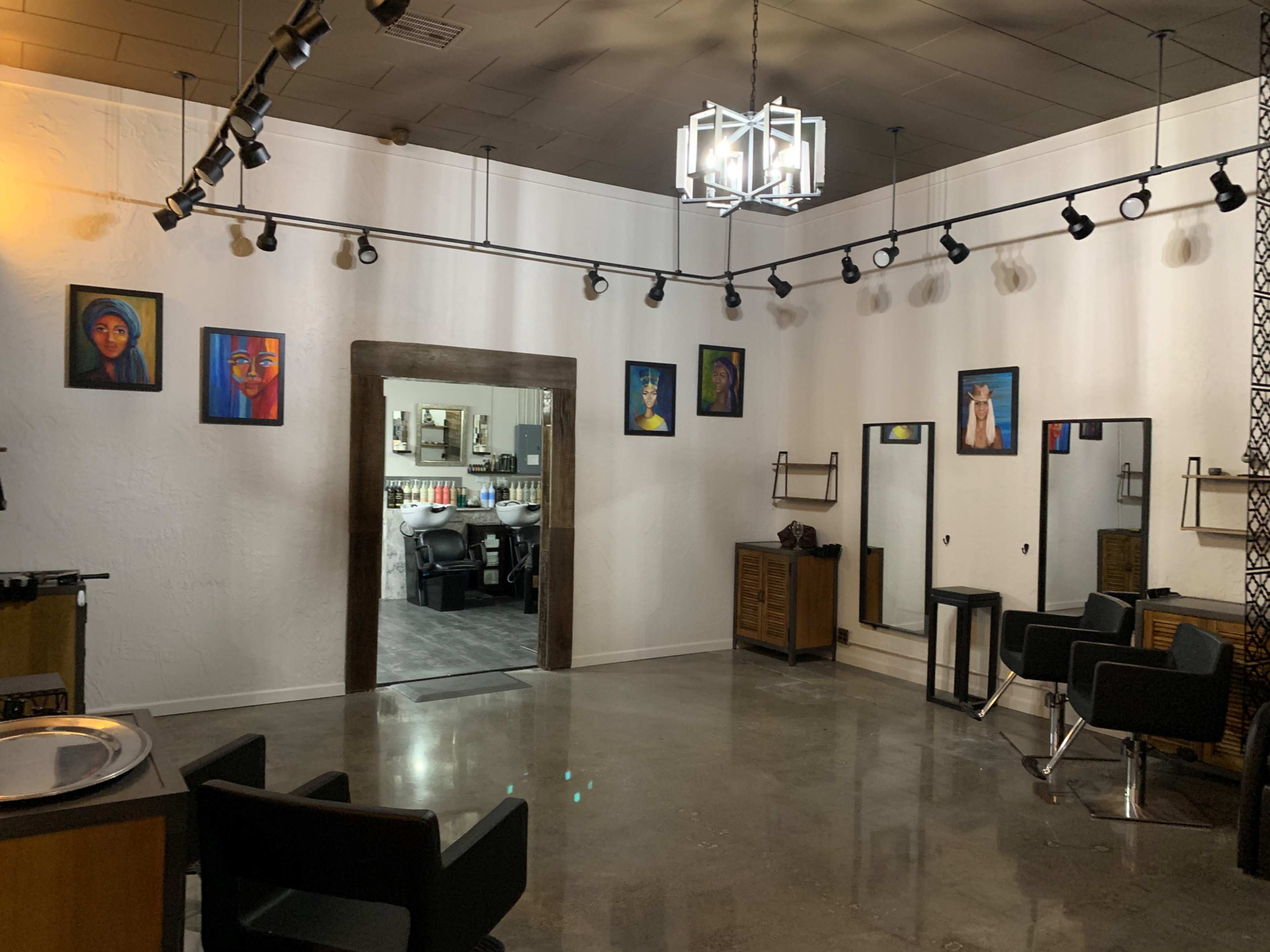 A modern hair salon with black chairs, a mirrored area, and artwork on the walls.