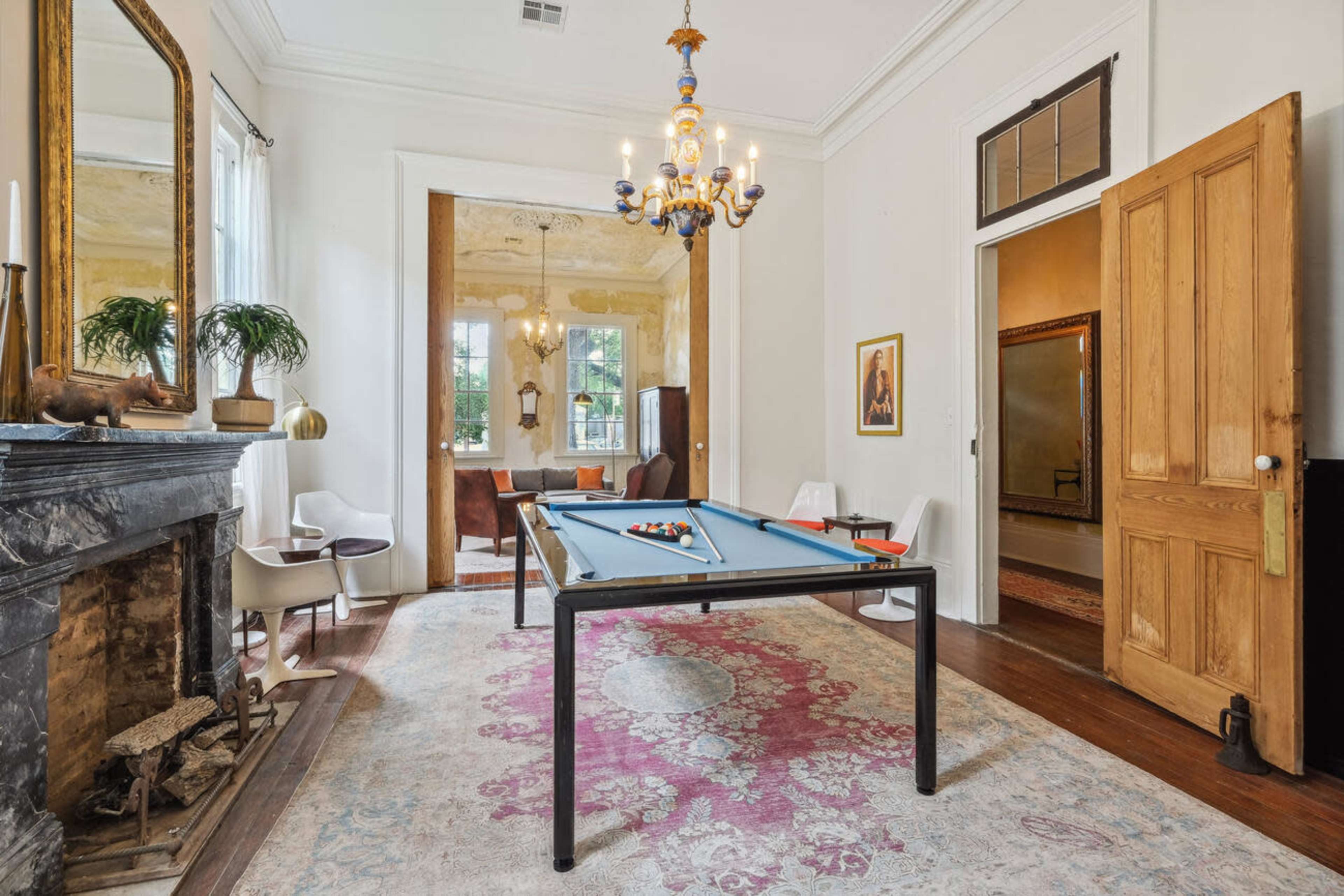 A game room features a pool table in the center, surrounded by a vintage fireplace and a doorway leading to a sitting area.