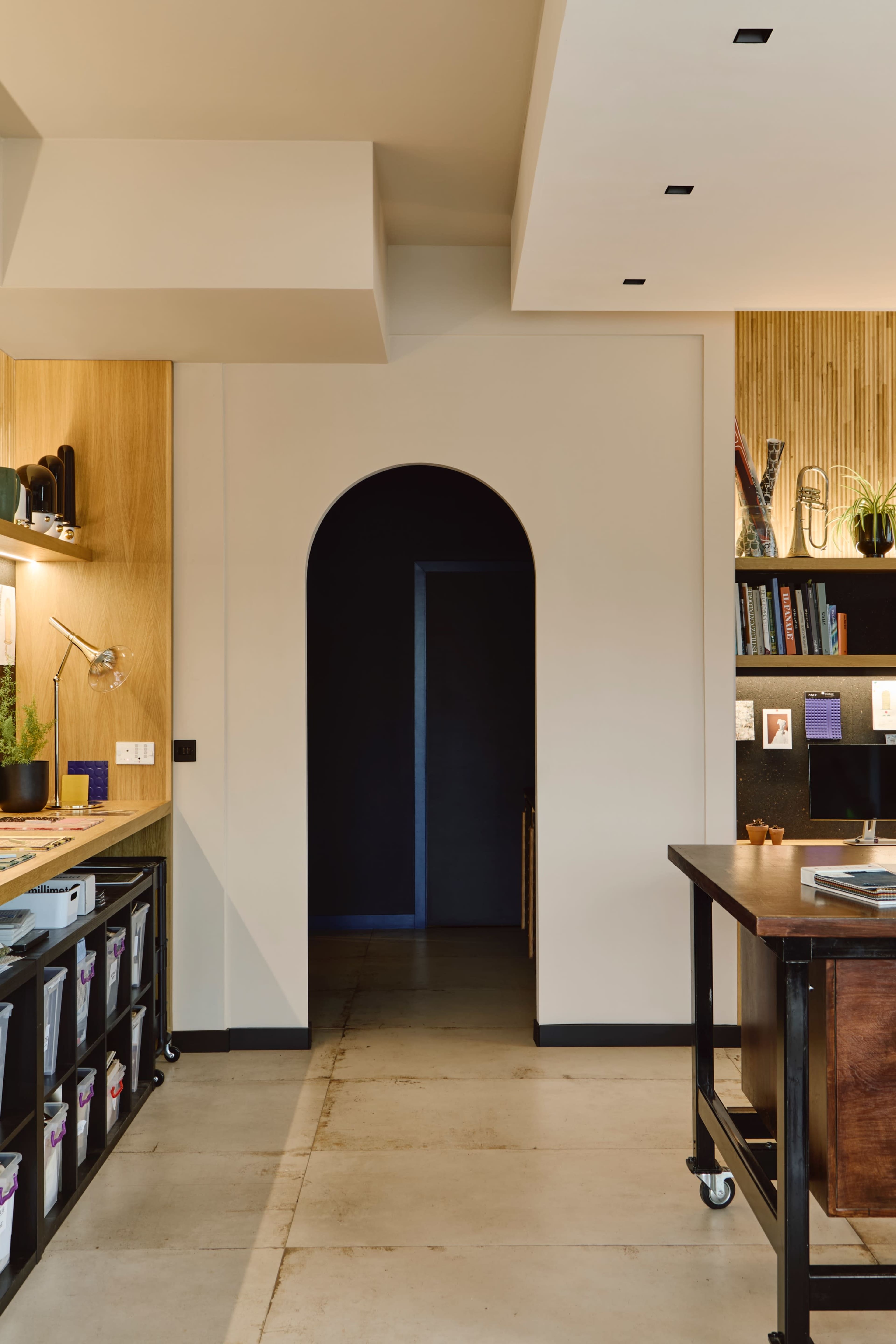 A modern interior space featuring an arched doorway, a wooden counter with storage bins, and a backdrop of shelves against a textured wall.