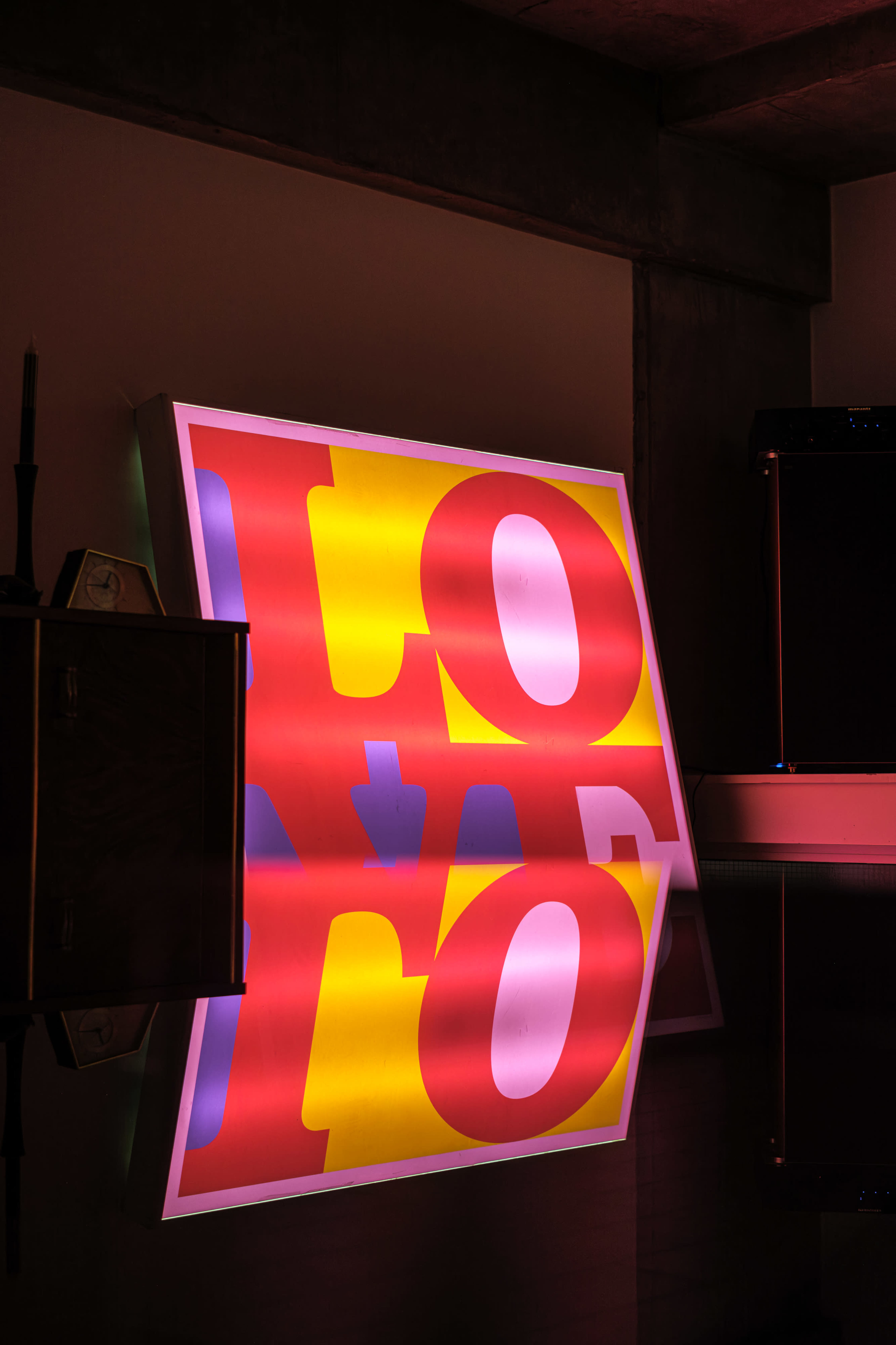 A brightly lit sign displaying the word "LOVE" is reflected on a glossy surface in a dimly lit room.