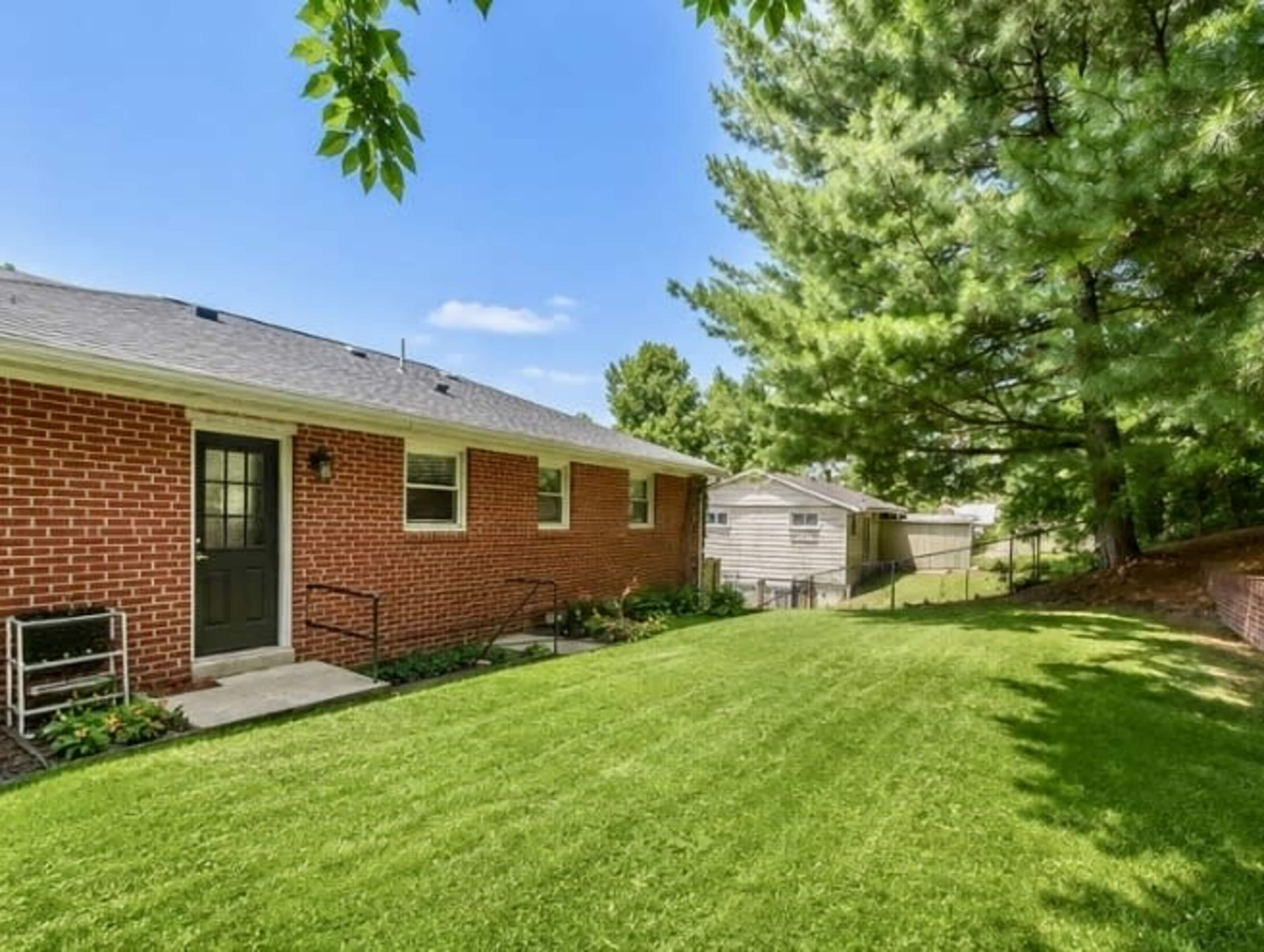 The image shows a brick house with a neatly maintained lawn and trees in the background.