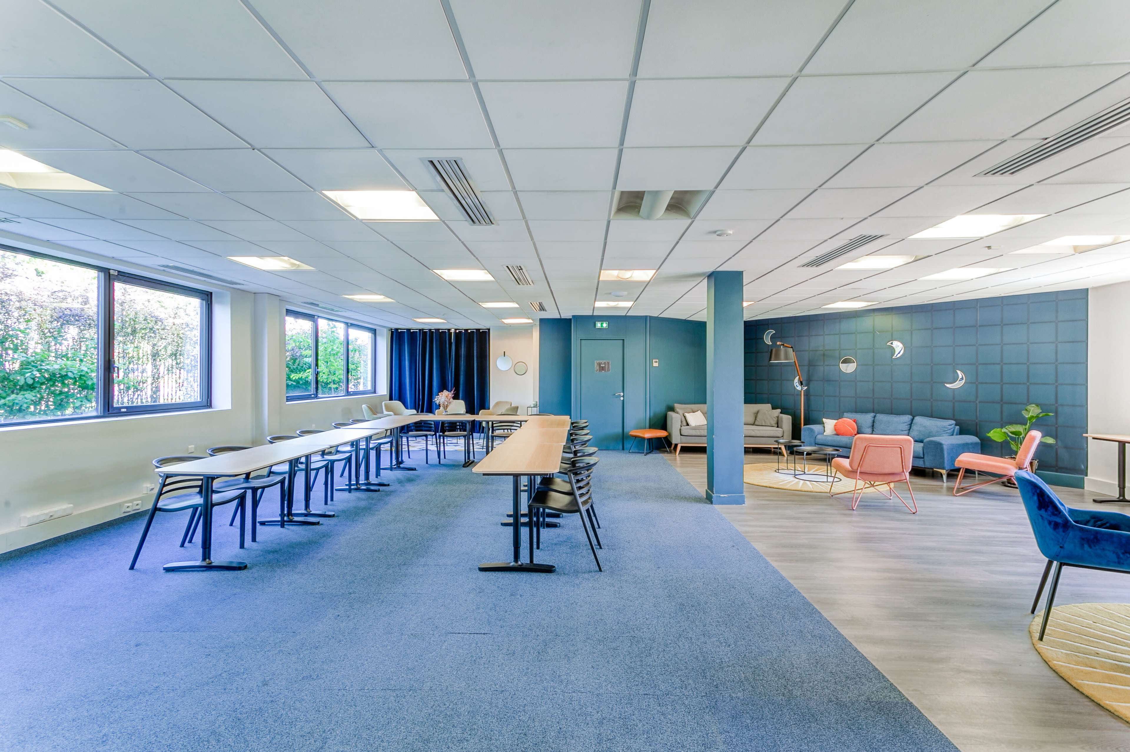 A modern office space with two distinct areas: a row of tables and chairs on the left and a lounge area with sofas and armchairs on the right.