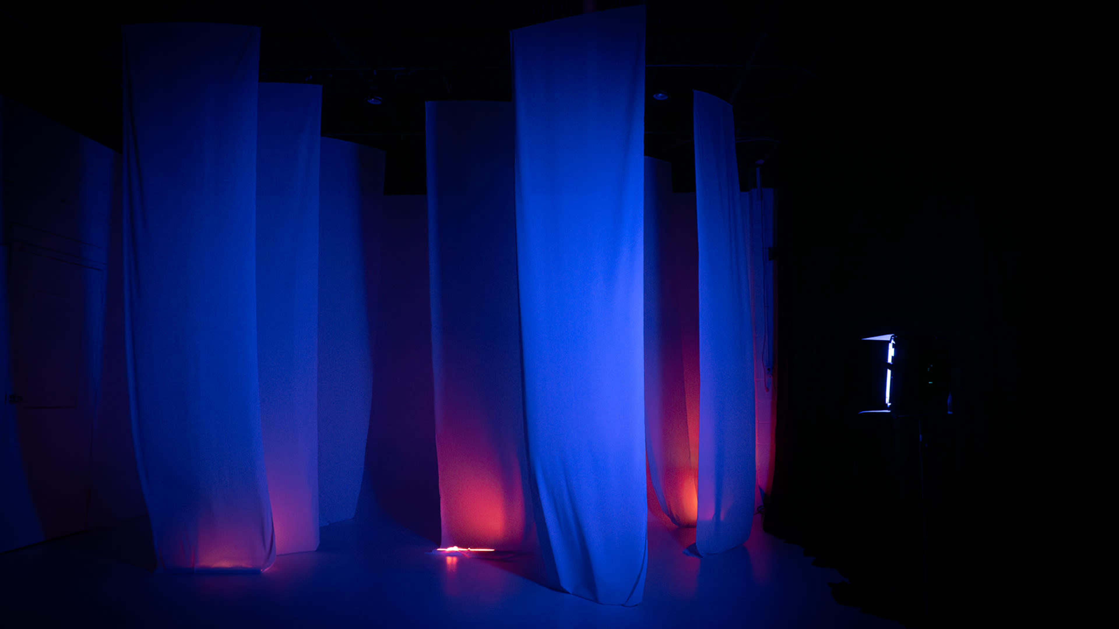 The image shows a dimly lit room with flowing fabric panels illuminated by blue and red lights.