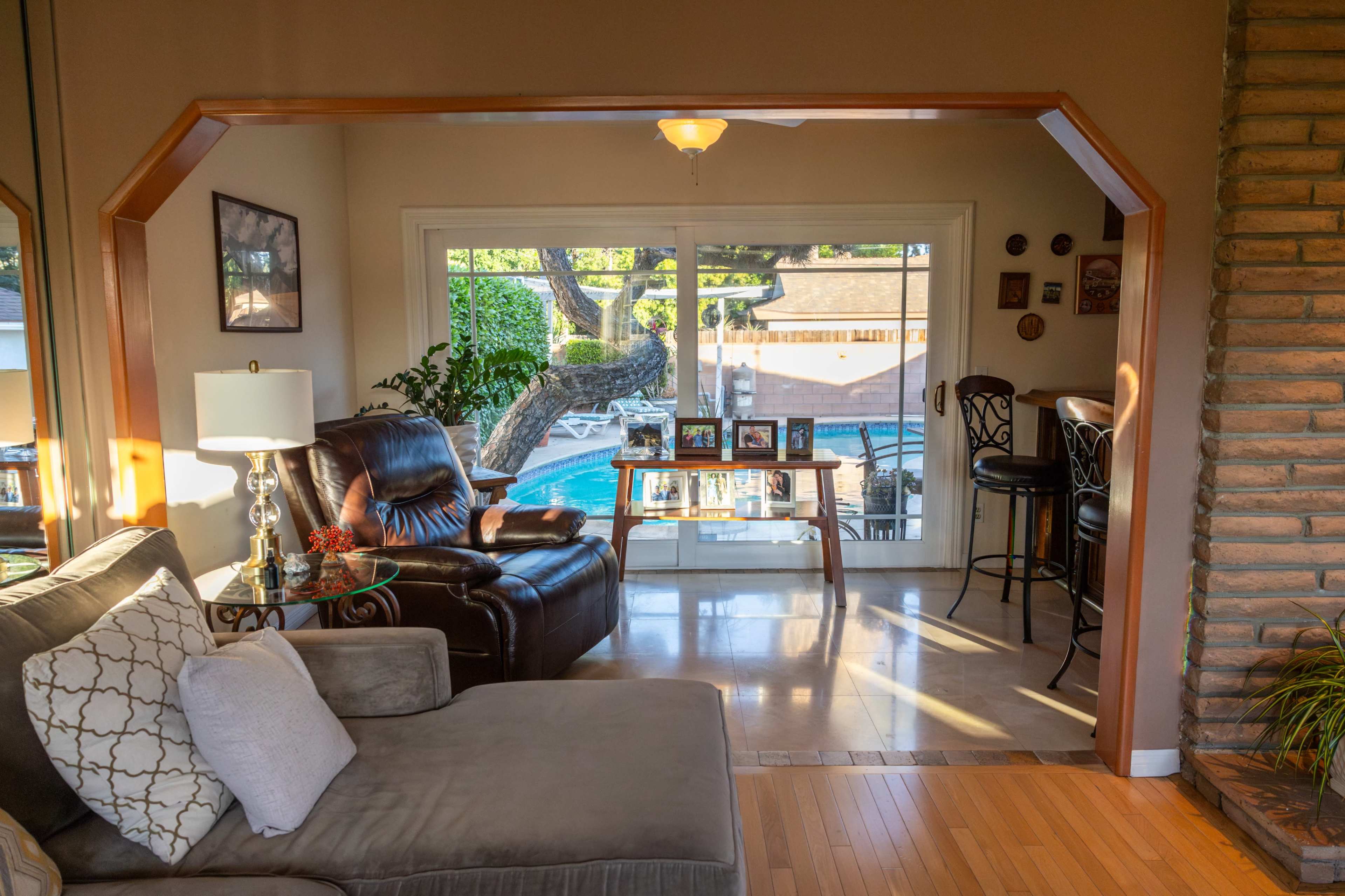 A living room with a view of a backyard pool, featuring a comfortable sofa, an armchair, and a glass table.