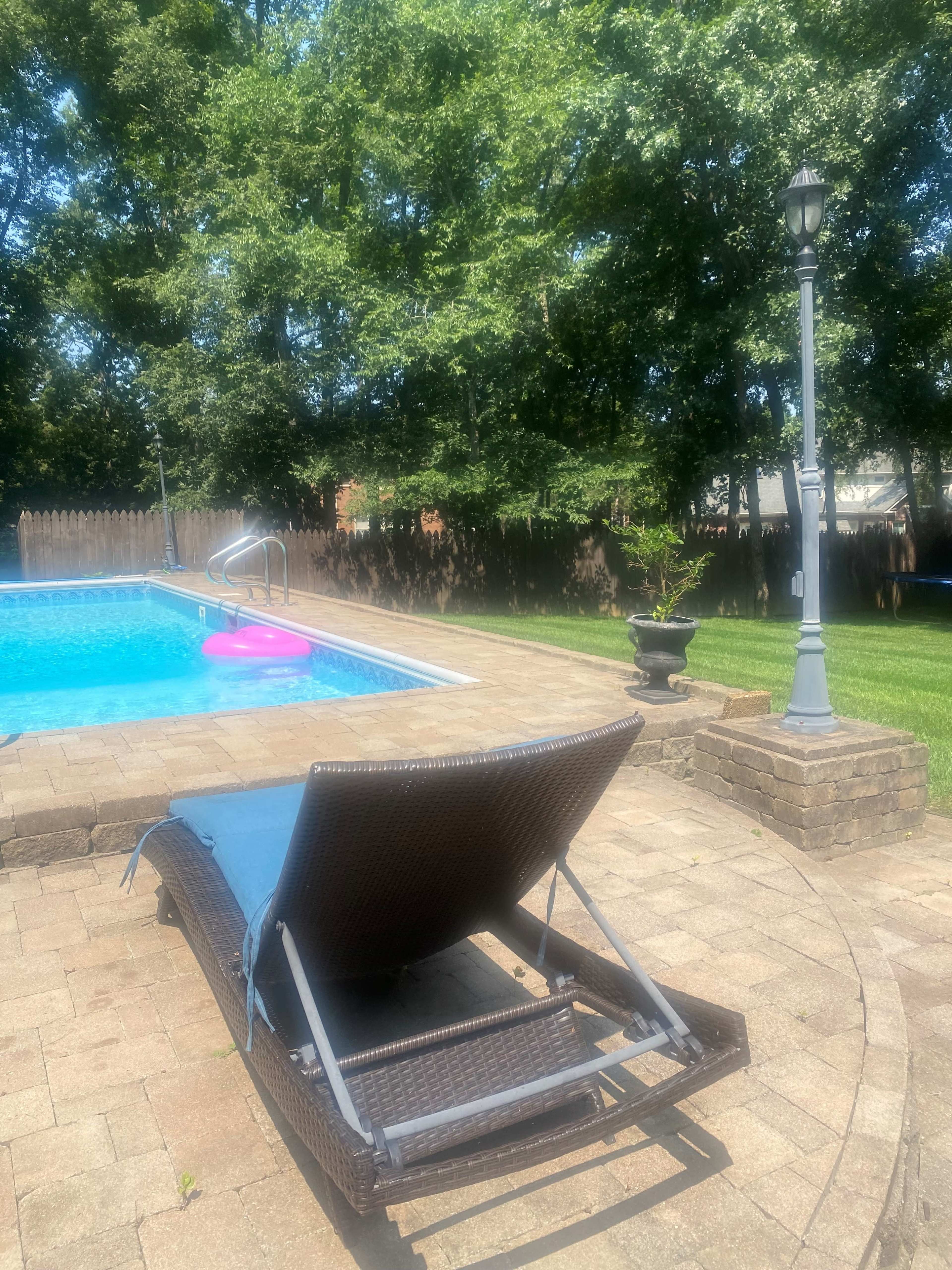 A lounge chair is positioned beside a swimming pool, with a pink float in the water and a lamp post nearby.