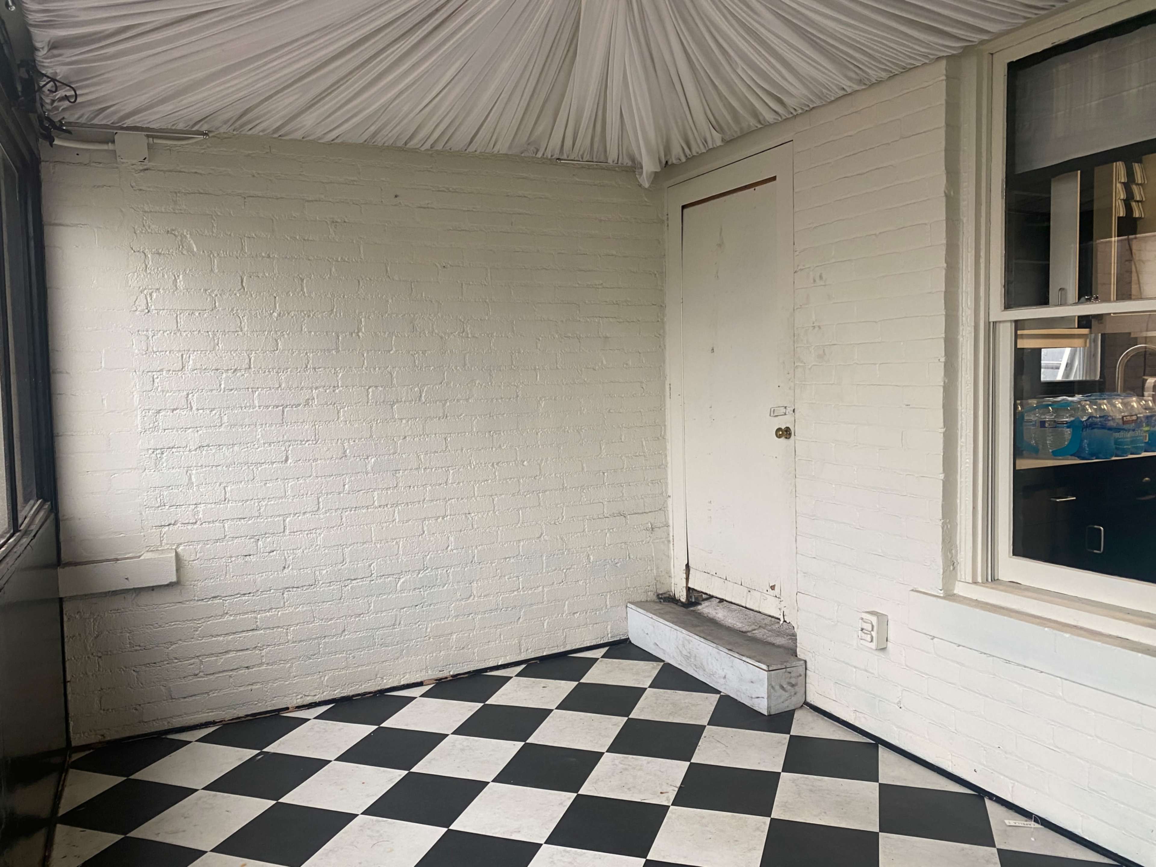 A small, enclosed space with white brick walls, a door on one side, and a checkered black and white floor.