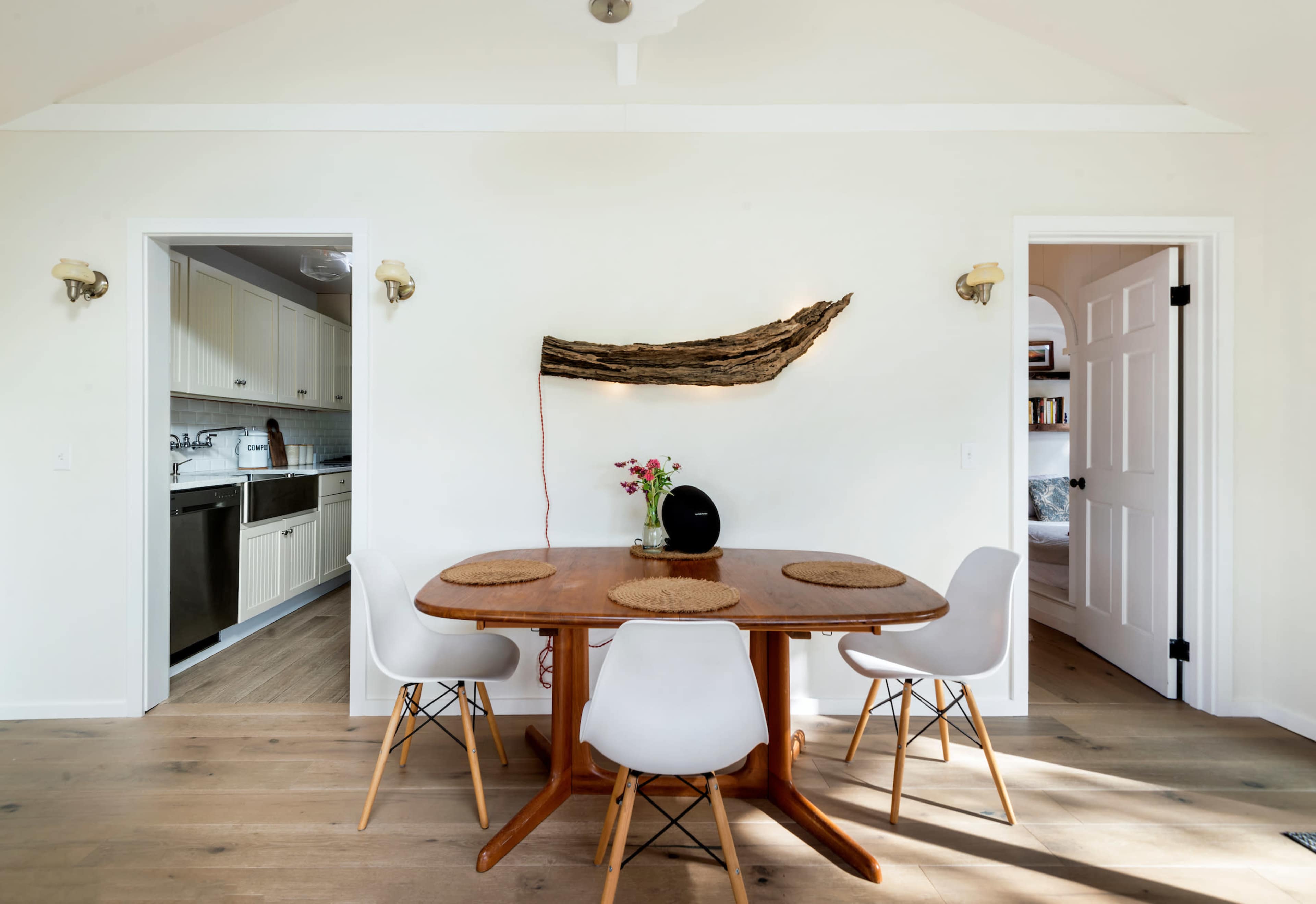 A dining area features a wooden table with four chairs, flanked by two doorways leading to kitchen and living spaces.