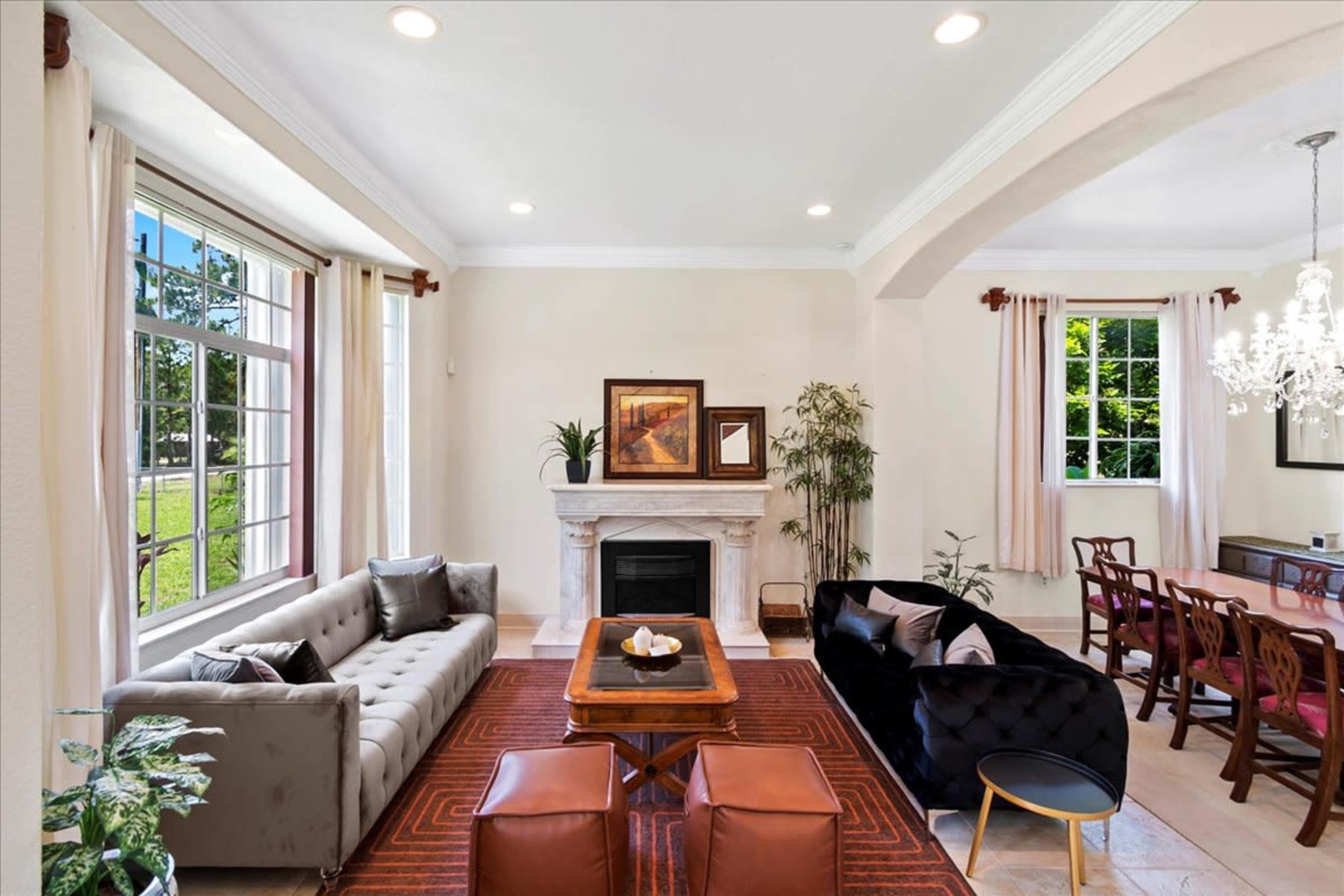 A well-lit living room featuring a gray sofa, a black velvet sofa, a coffee table, and a fireplace, with large windows allowing natural light to enter.