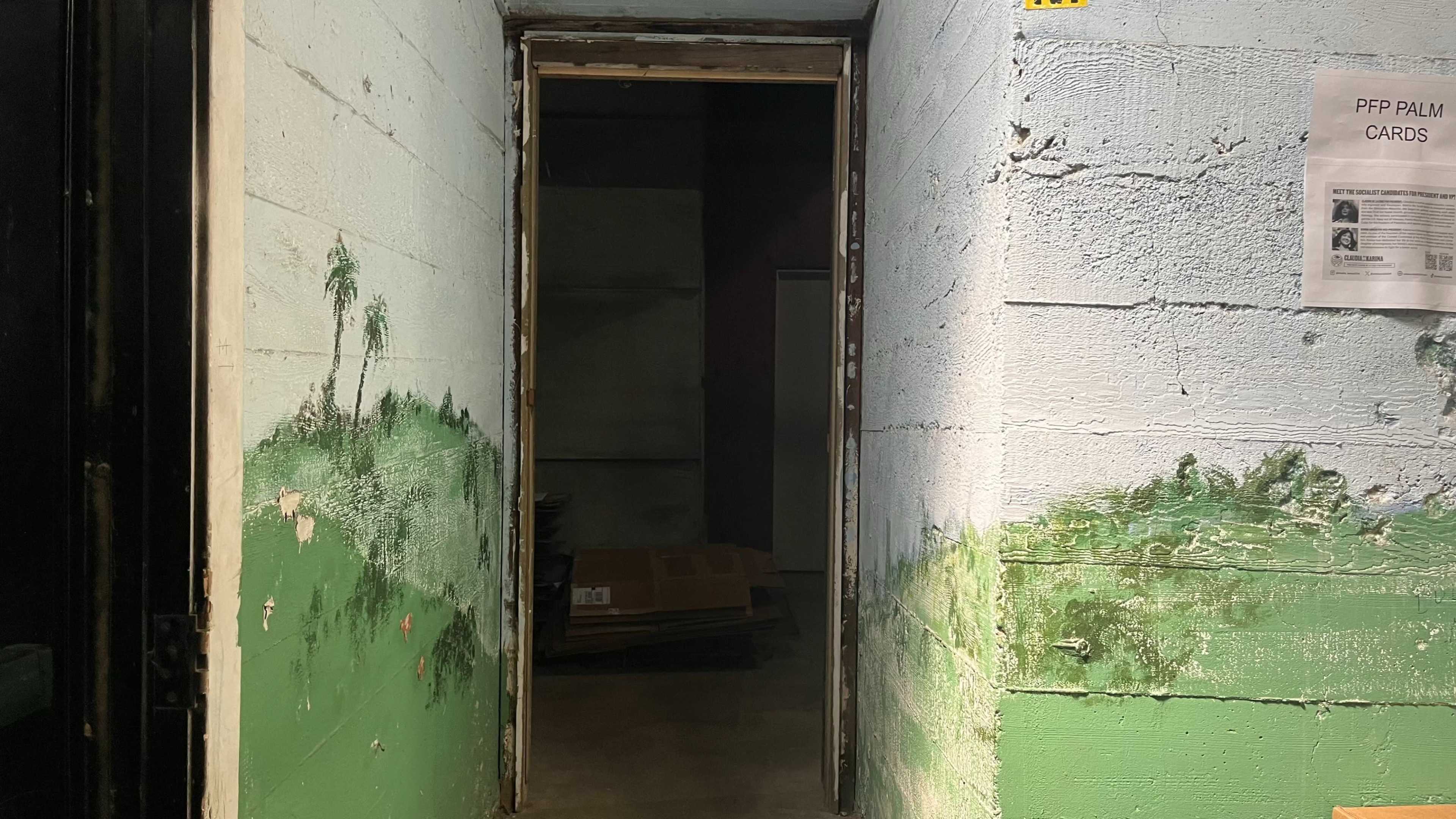 The image shows an open doorway leading into a dimly lit space with green-painted walls and a mural of palm trees.