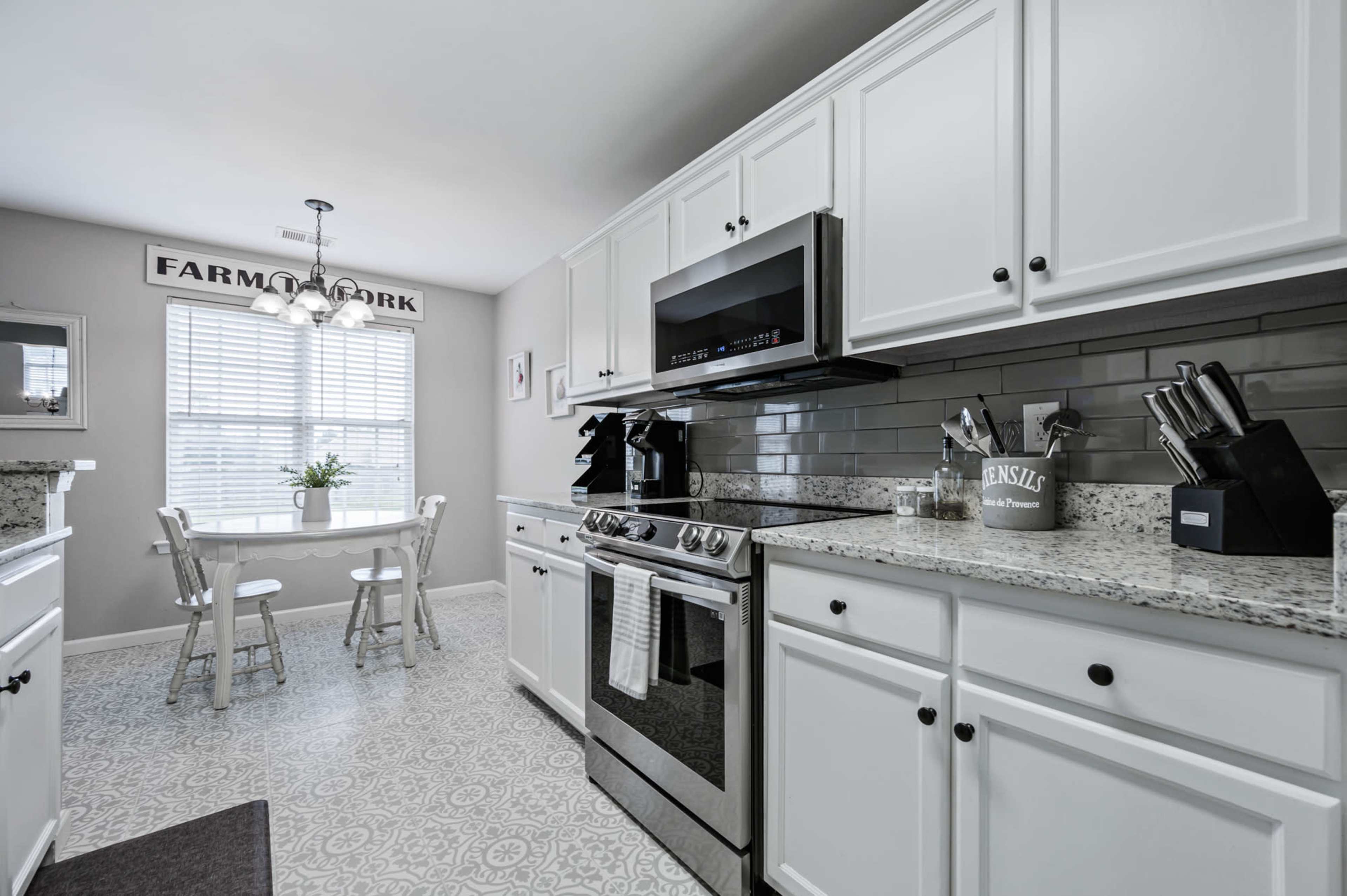 A modern kitchen features white cabinetry, stainless steel appliances, and a small dining table with chairs near a window.