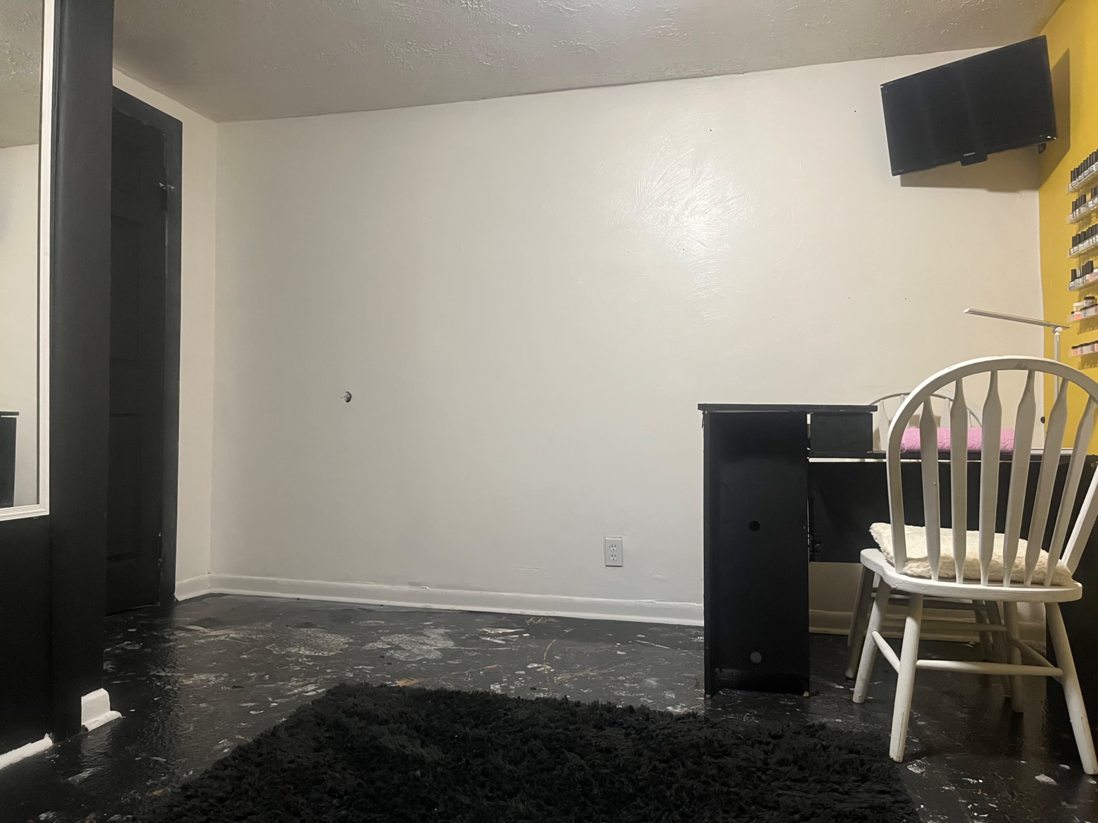 A sparsely furnished room with a desk and chair, a large mirror, and a television mounted on the wall.