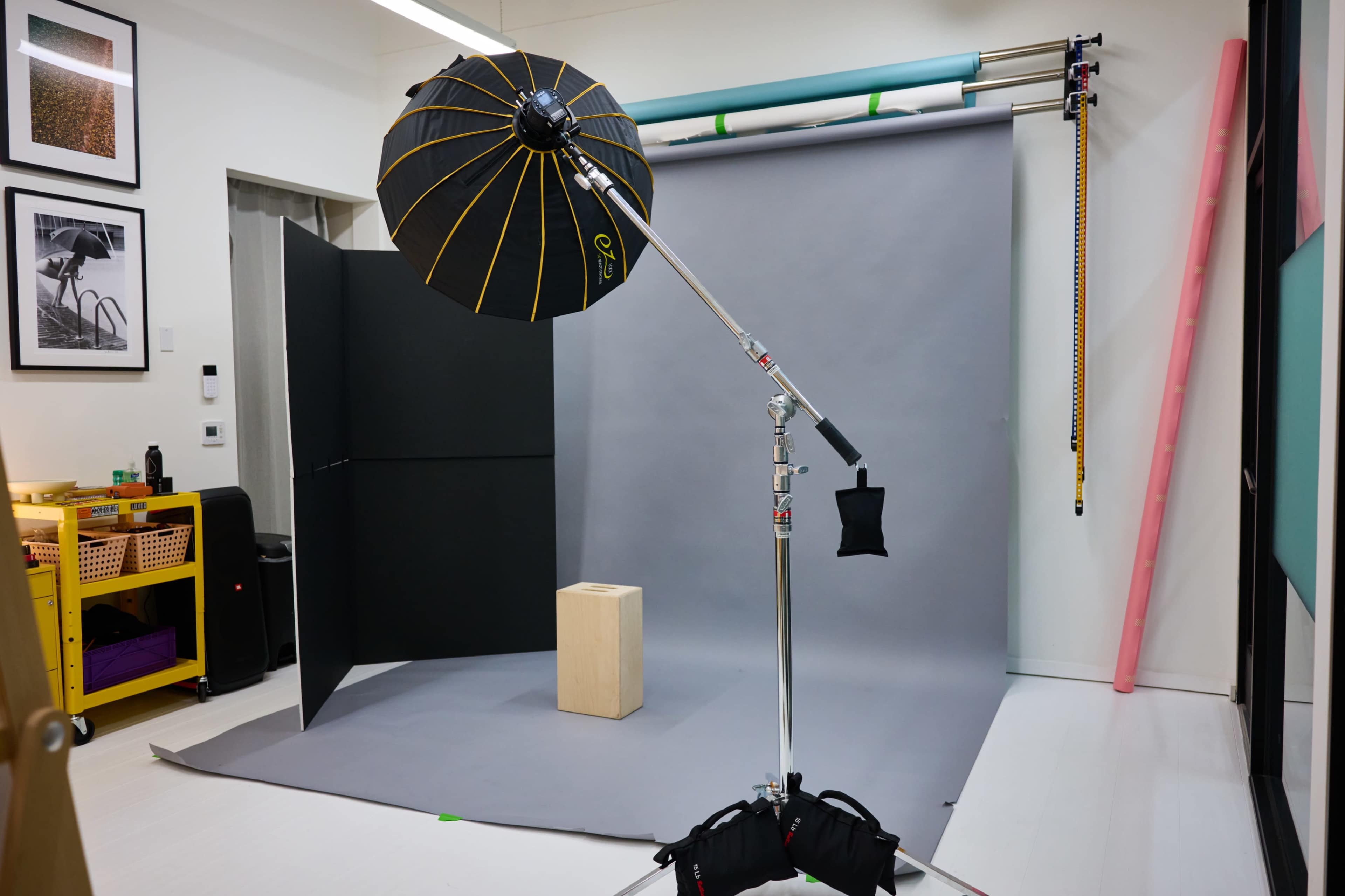 A photography studio setup featuring a softbox on a stand, a gray backdrop, a wooden prop, and various lighting equipment.