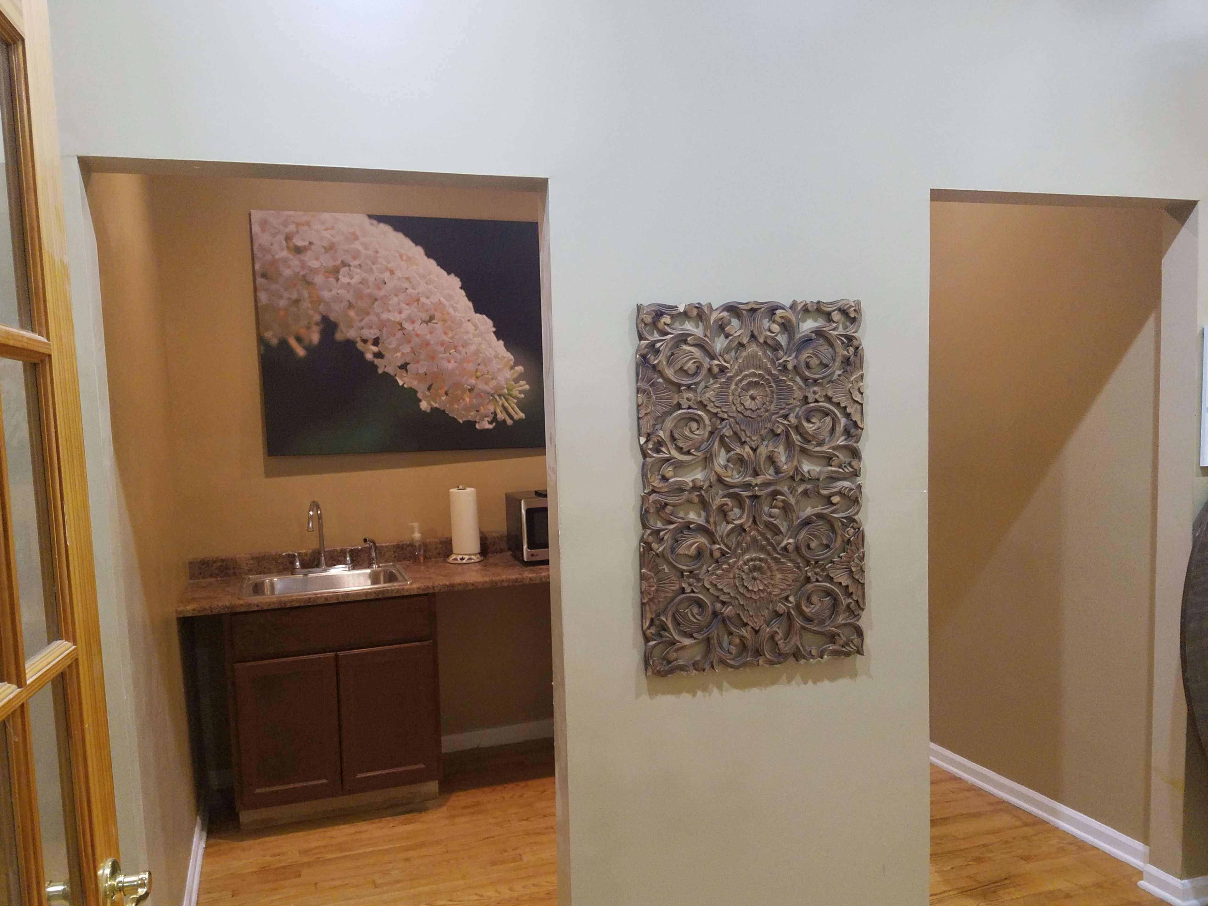 A hallway with a small kitchenette on the left and a textured wall decoration on the right.