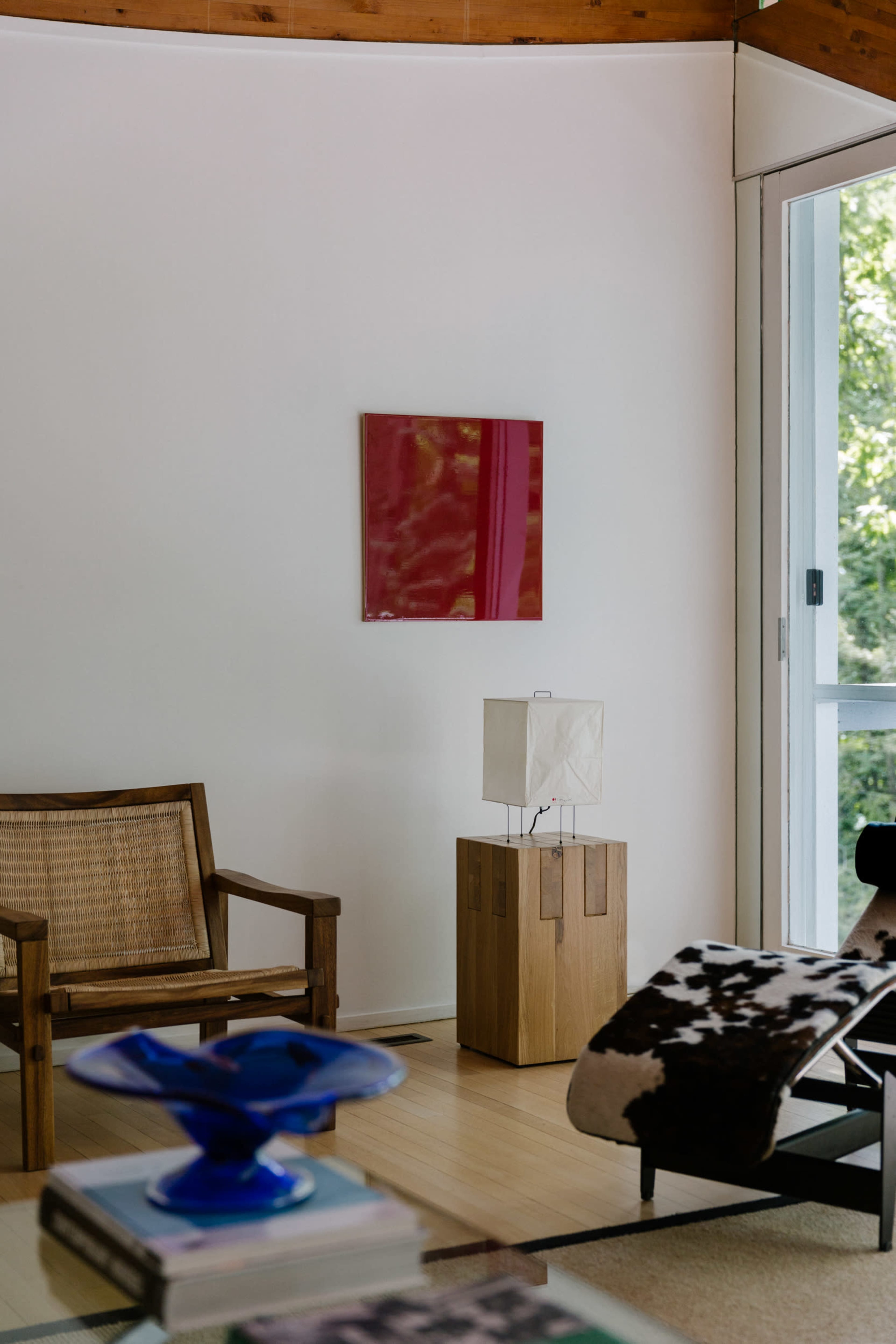 A minimalistic living room featuring a chair, a lamp on a wooden stand, and abstract artwork on the wall.