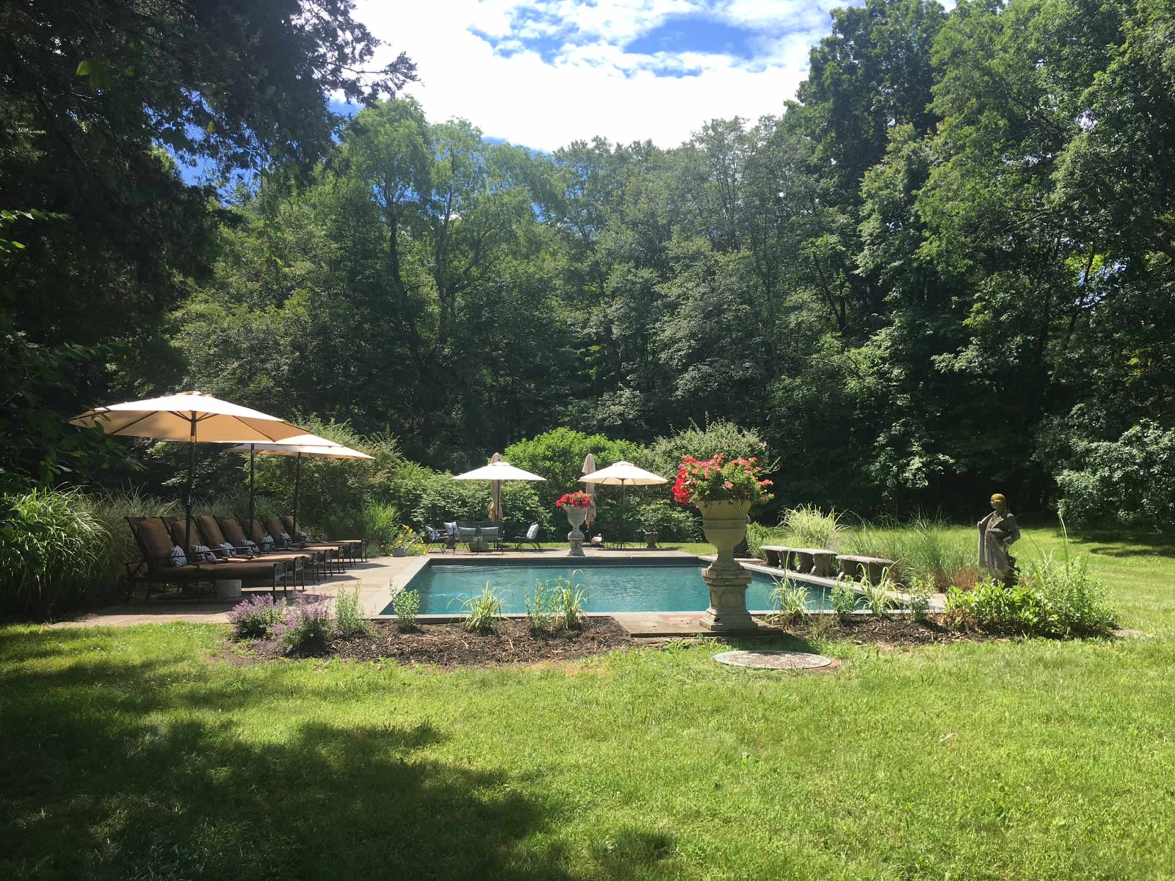 The image shows a well-maintained pool area surrounded by lounge chairs, umbrellas, and landscaped greenery.