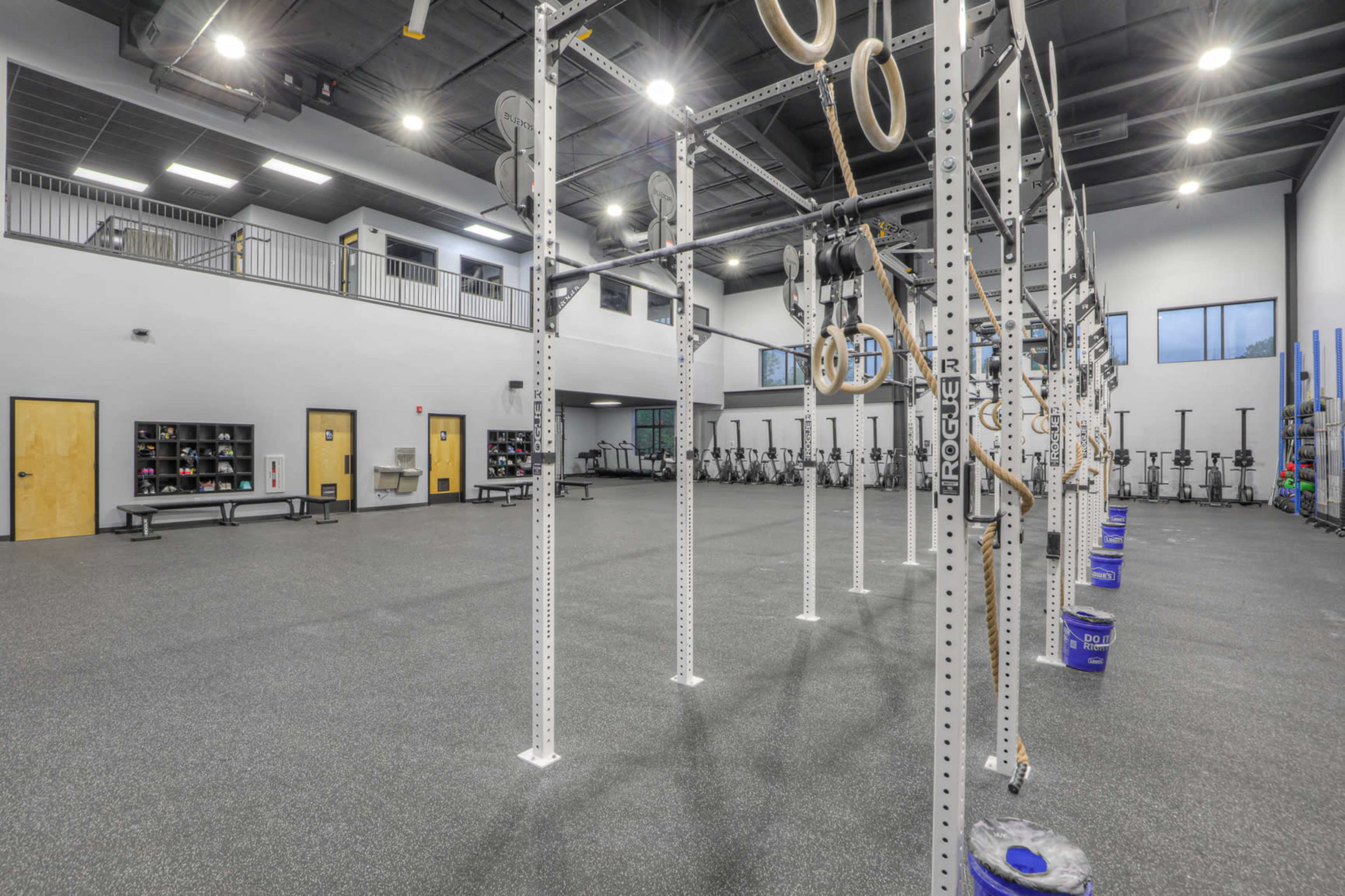 The image shows a spacious gym with a rig for exercise equipment and various fitness stations lined against the walls.