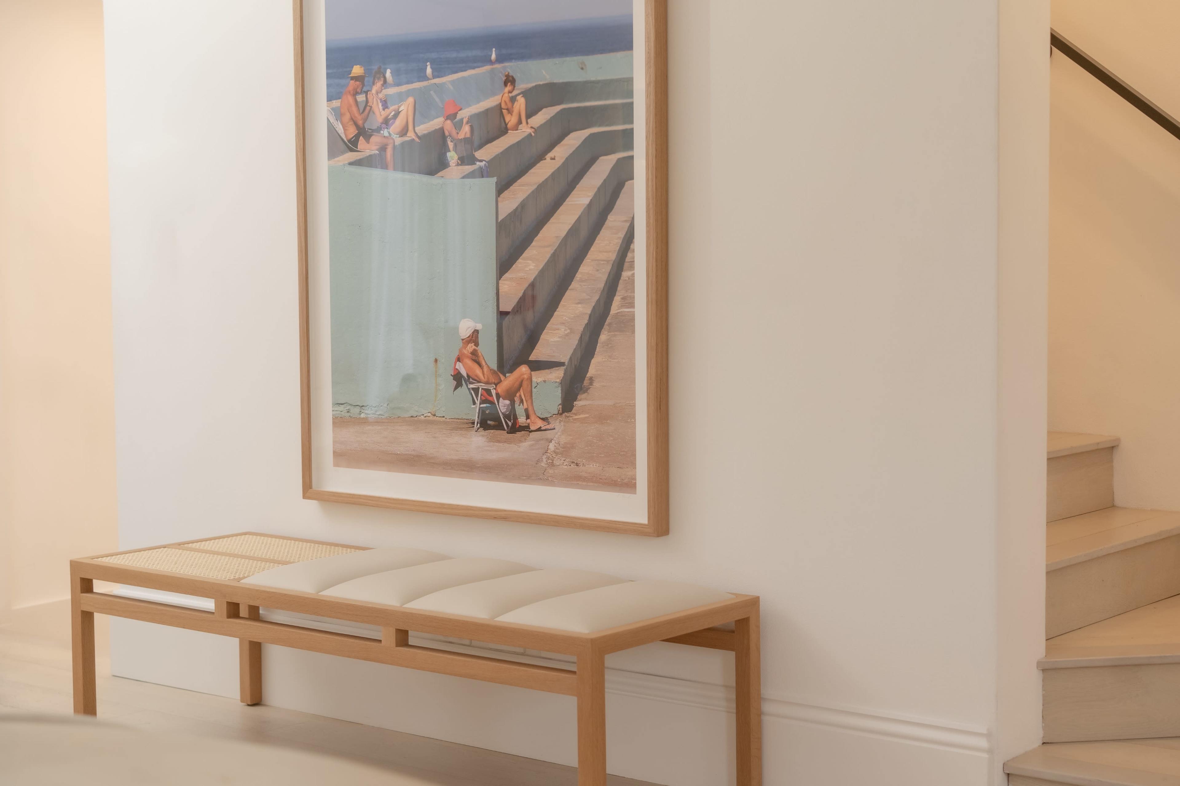 The image features a wooden bench positioned next to a large framed photograph of people relaxing by a pool, with stairs visible in the background.